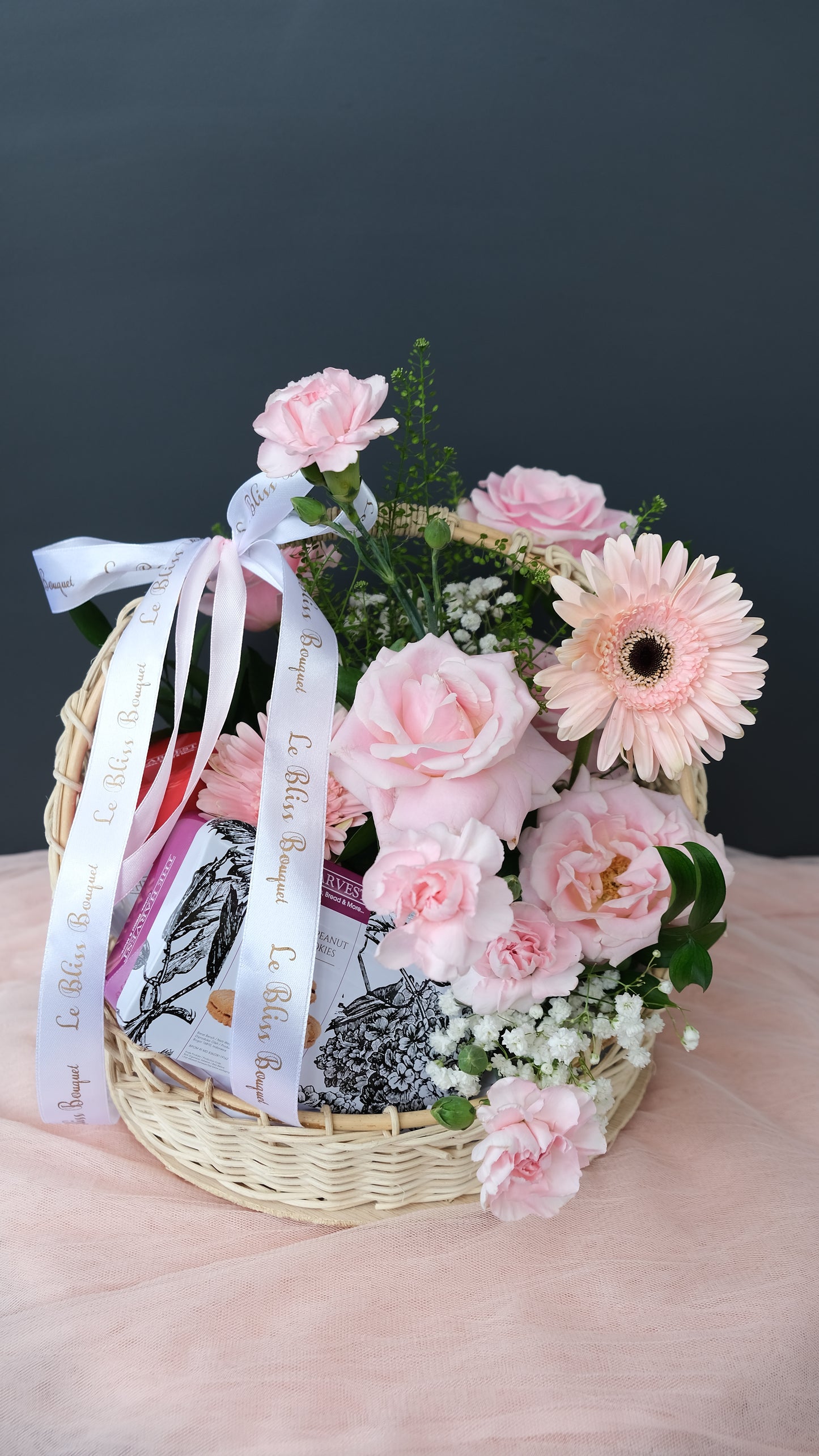 Cookies hamper in rattan basket decorated with a pink flower ring, perfect for gifting. Available for delivery in Jakarta, Bintaro, Tangerang, and Cirebon. by Le Bliss Bouquet