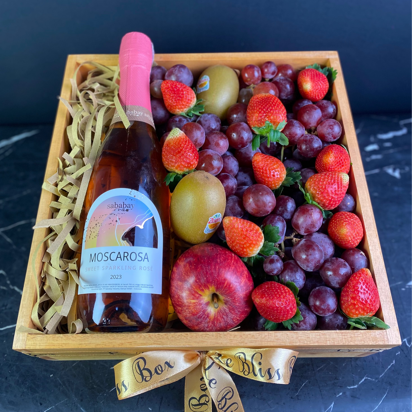 Fruit basket with a bottle of Moscarosa wine on a dark surface. sababay wine hamper jakarta, wine hamper surabaya, sababay wine