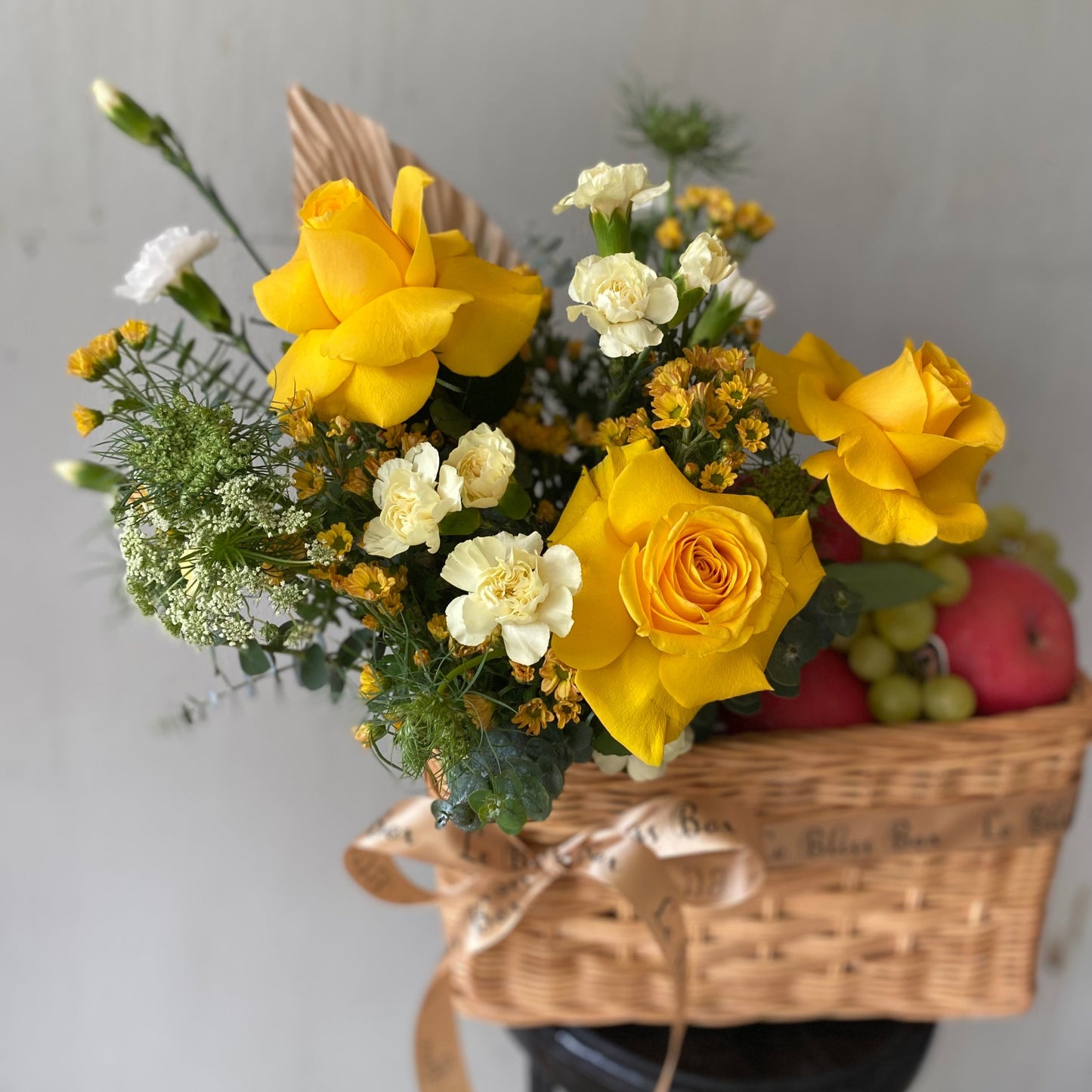 Keranjang anyaman cantik berisi buah-buahan segar dan bunga mawar kuning yang memikat, dipegang oleh seorang wanita dengan kemeja merah muda. Tersedia untuk pengiriman di Jakarta, Bintaro, Bogor, Bekasi, dan Depok.