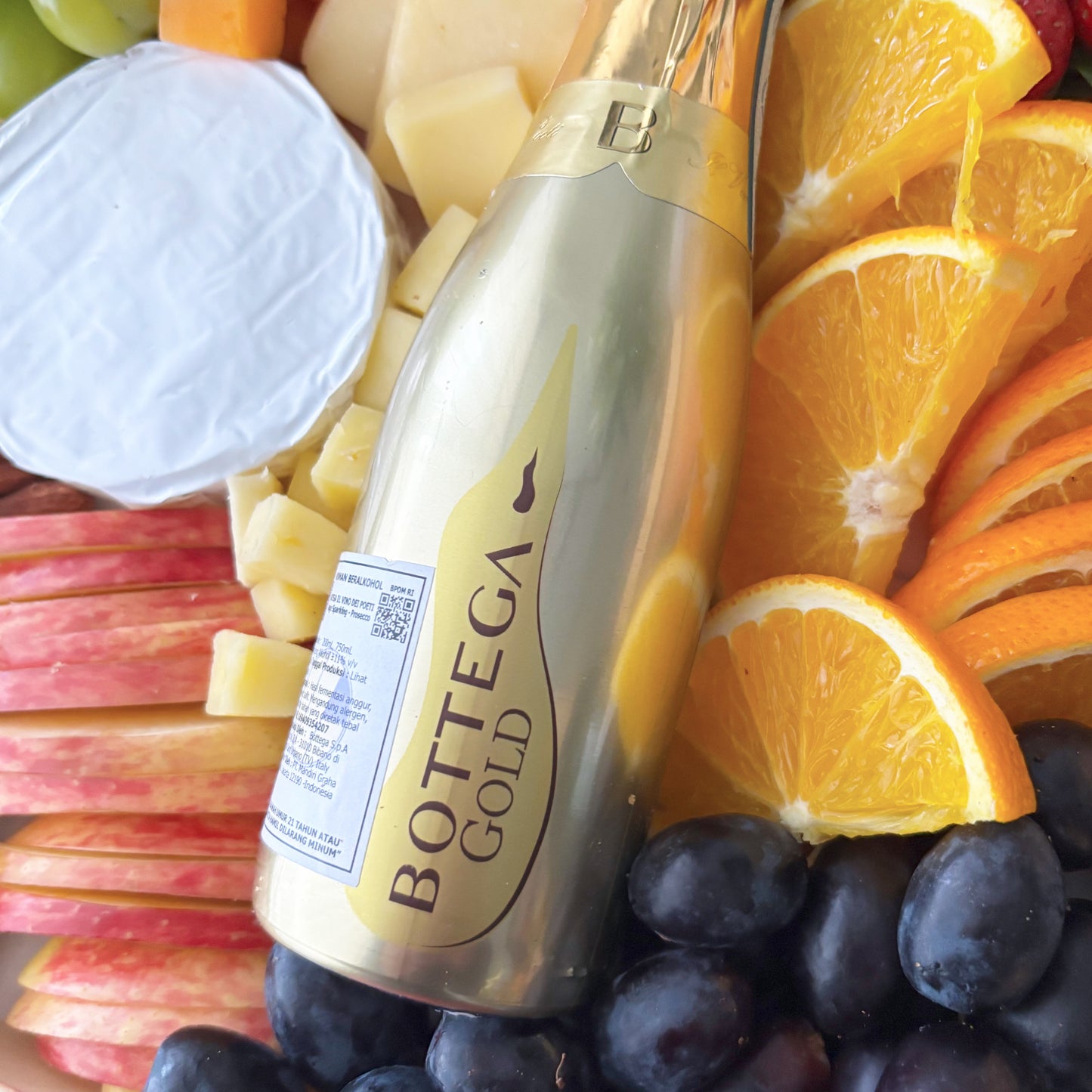 Bottle of Bottega Gold champagne surrounded by fruits and cheese on a platter