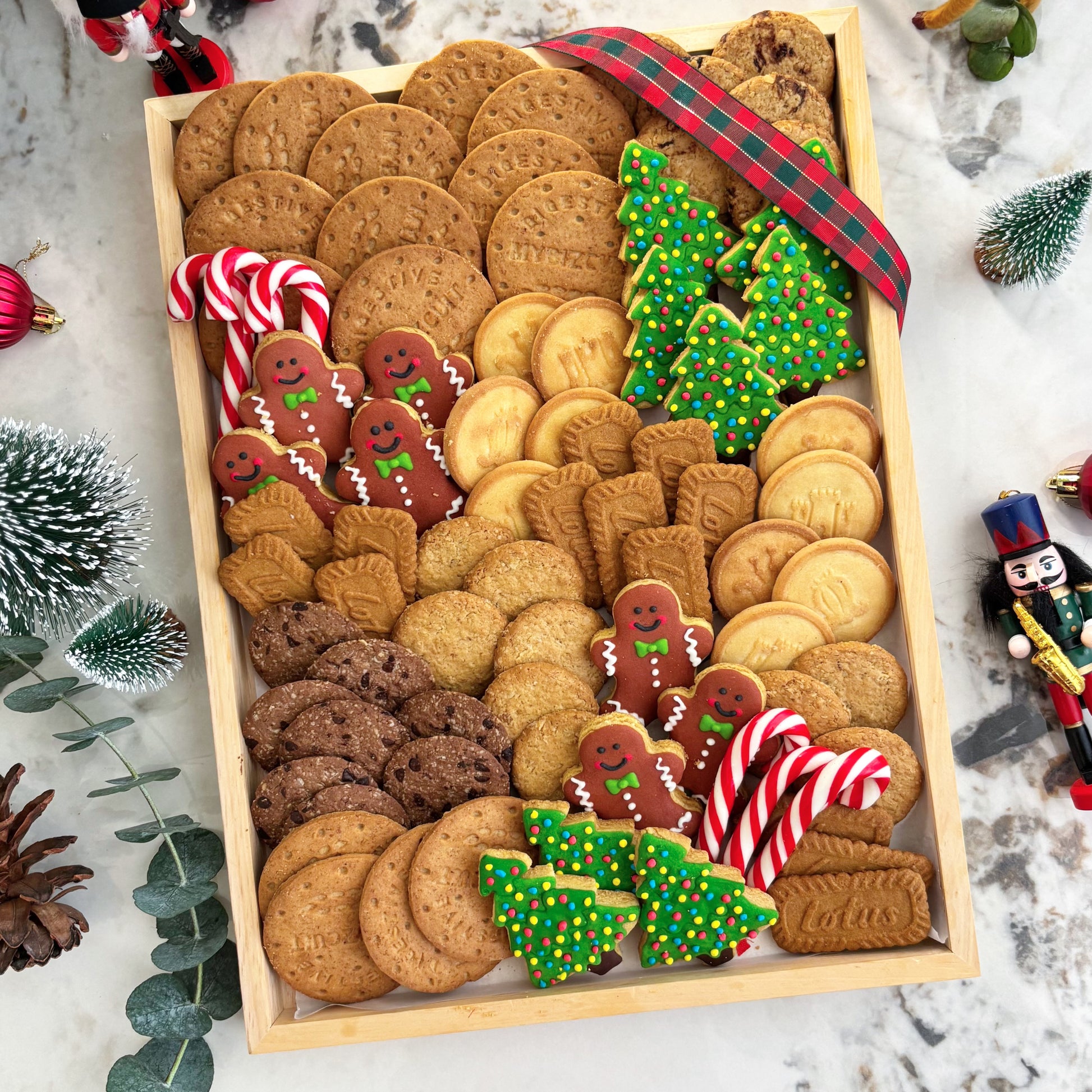 Assorted Christmas cookies in a wooden box with decorative elements on a marble surface. Celebrate Christmas with Le Bliss Platter’s Cookies Platter — festive cookies & treats beautifully arranged. Available for delivery in Jakarta & Surabaya.