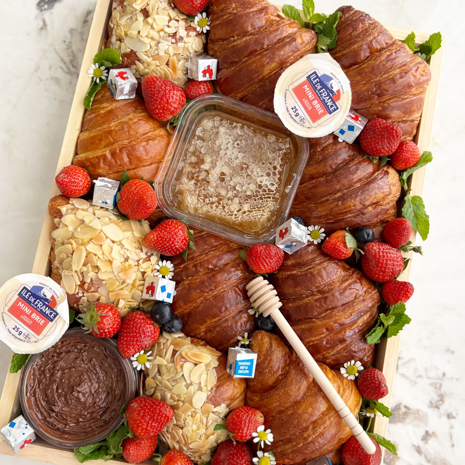 Assorted croissants with fruits and pastries on a marble surface. Wooden box of croissants with various toppings on a marble surface. Croissant Platter with cheese honey, cheese platter jakarta, cheese platter surabaya