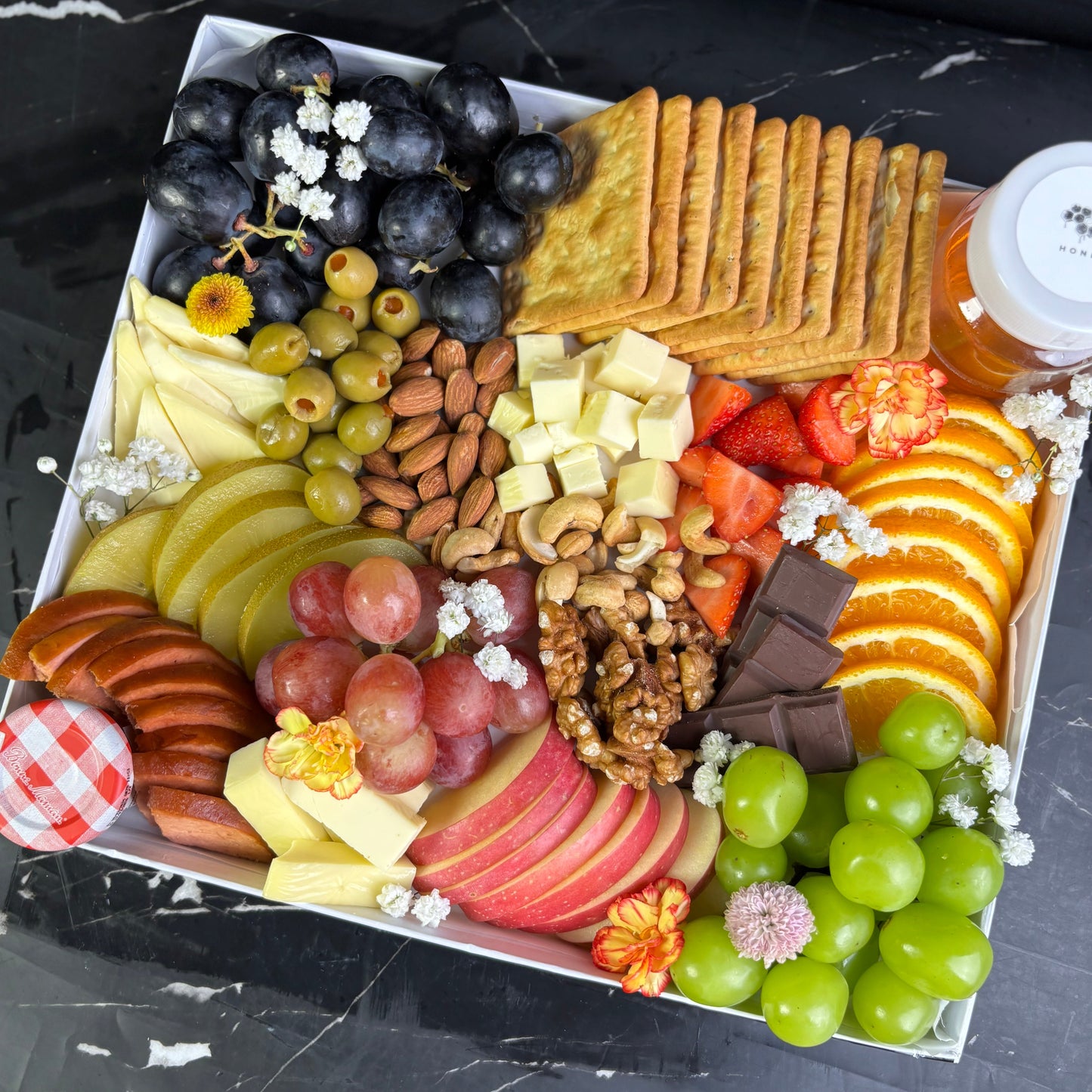 Assorted fruits, cheeses, and crackers on a black marble surface. vegan cheese platter jakarta dan surabaya
