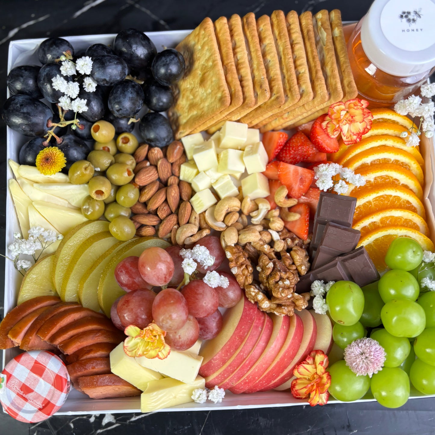 Assorted fruits, cheeses, and crackers on a platter with a bottle of wine in the background. vegan cheese platter surabaya, Jakarta by le bliss platter