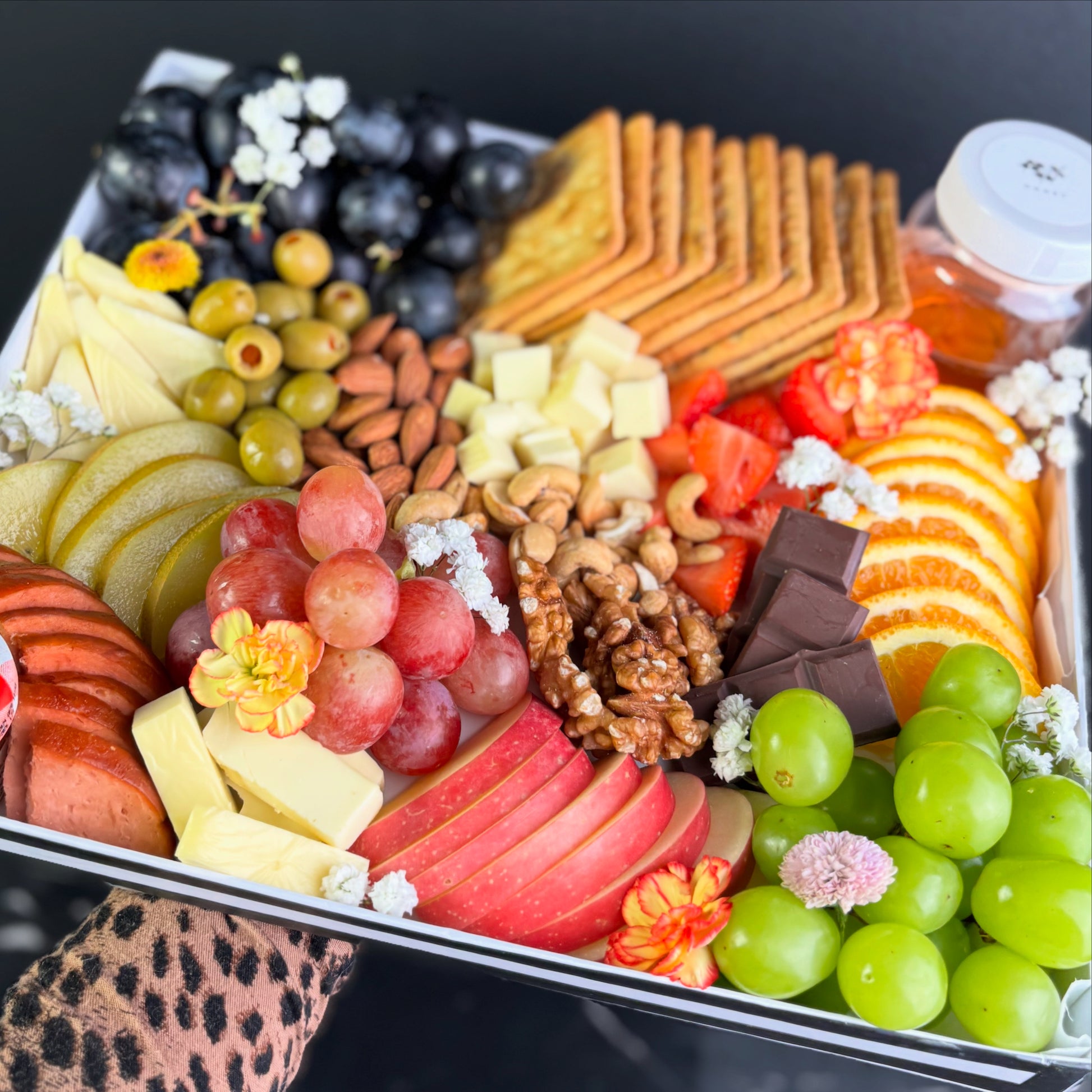Assorted fruits, cheeses, and crackers on a platter with decorative elements. Vegan cheese platter by le bliss platter