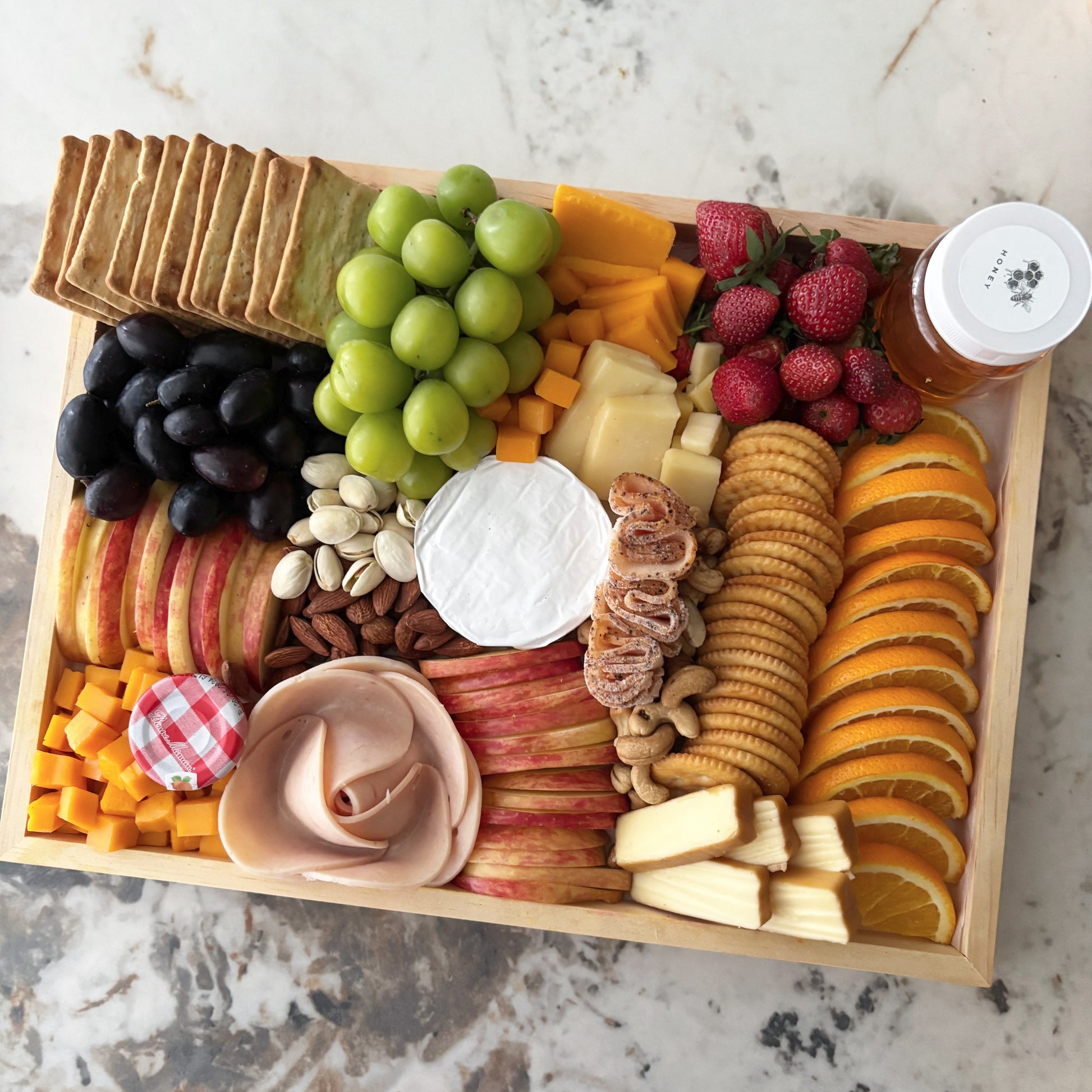 Assorted fruits, cheeses, and crackers on a wooden tray with a marble background, chicken salami, chicken pastrami, cheese platter jakarta, cheese platter surabaya