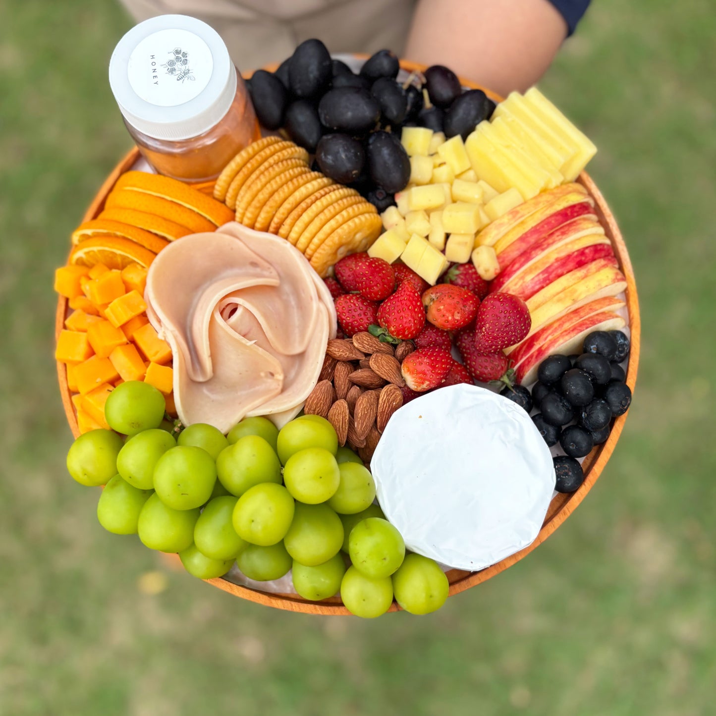 Assorted fruits, cheeses, and meats on a platter with a blurred green background. Assorted fruits, cheeses, and meats on a platter by le bliss platter. cheese platter jakarta, cheese platter surabaya, with chicken salami