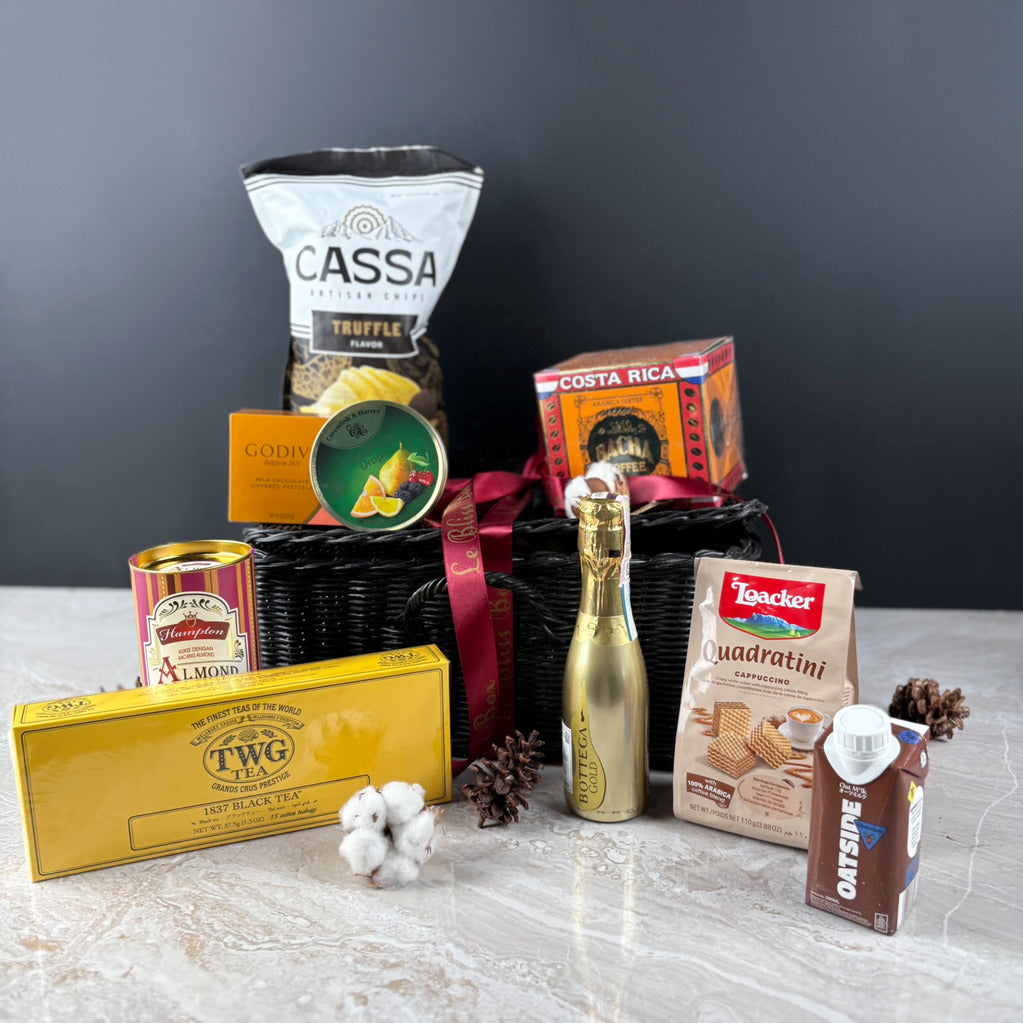 Assorted gourmet items including a bottle of champagne, tea, and cookies on a gray surface with a dark background. Gift basket with various items including a bottle, boxes, and snacks by le bliss box. a premium snack gourmet hamper in jakarta, surabaya, cirebon
