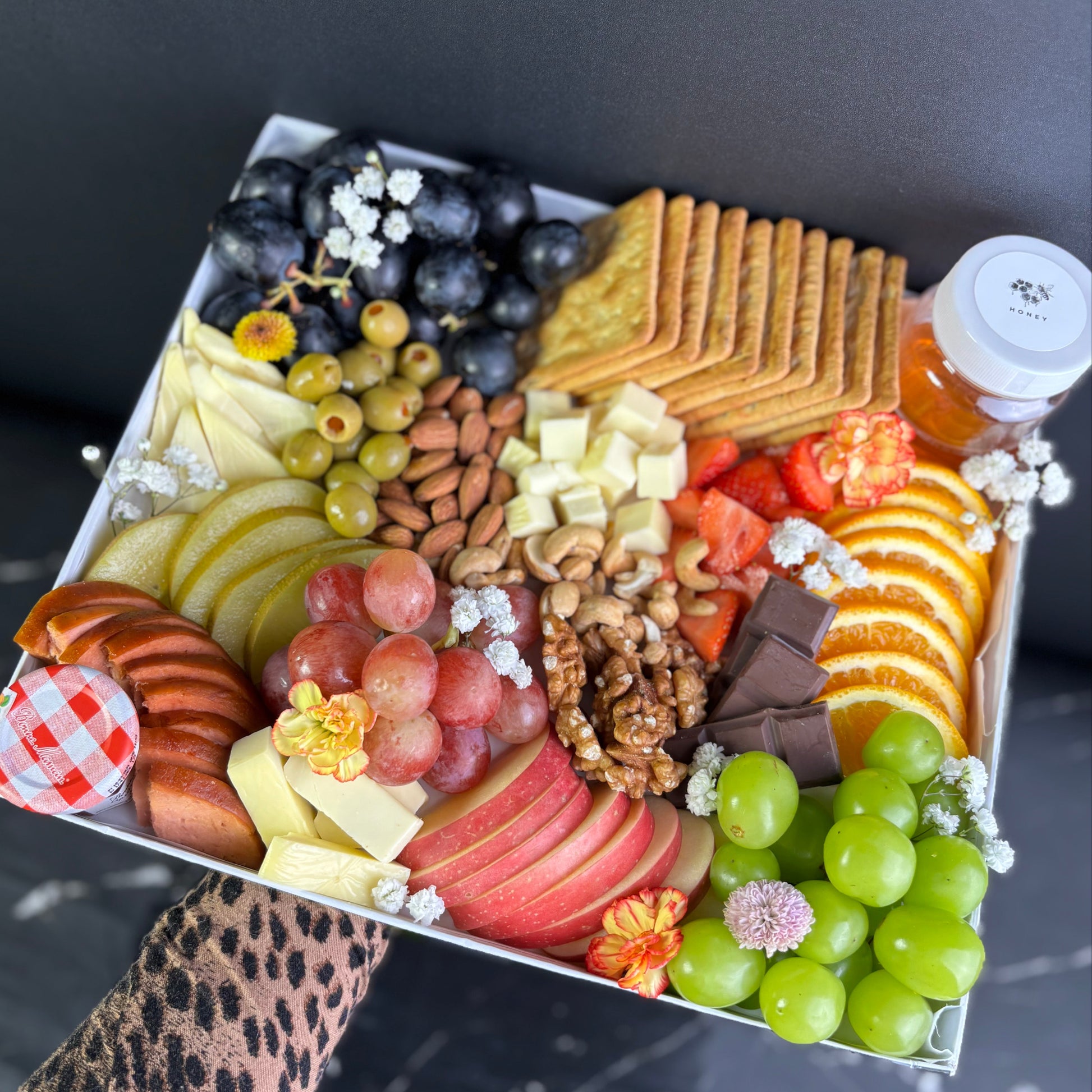 Assorted snack platter with fruits, crackers, and other treats on a dark surface. vegan cheese platter bintaro, tangerang, surabaya