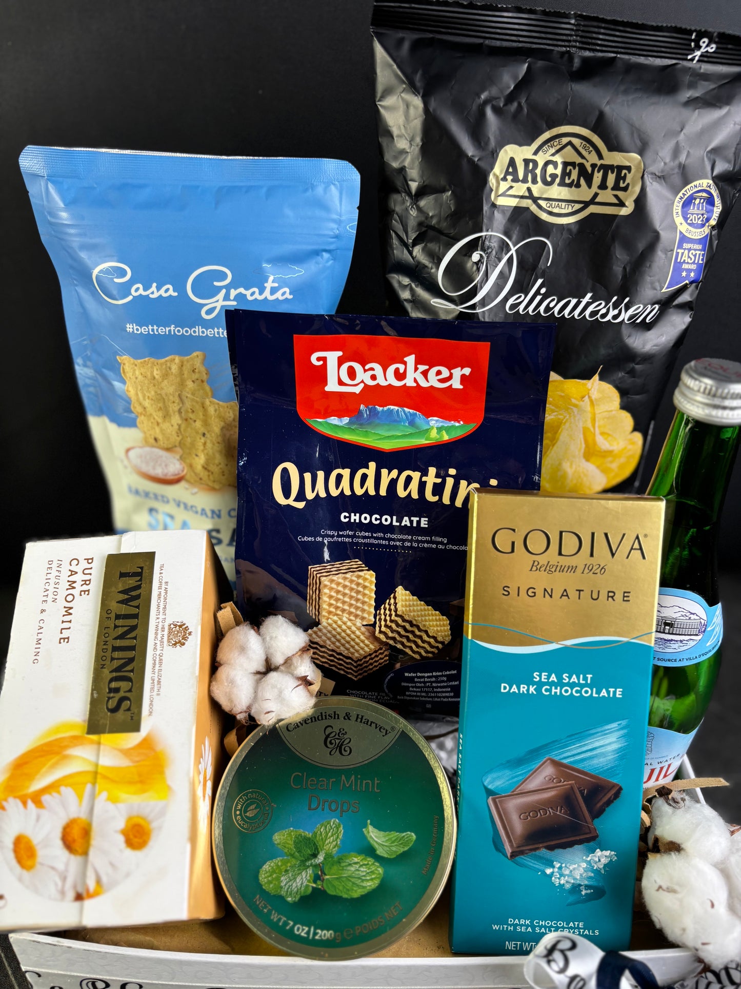 Assorted snacks and treats including chocolate, cookies, and a bottle on a dark background. Gourmet Hamper jakarta