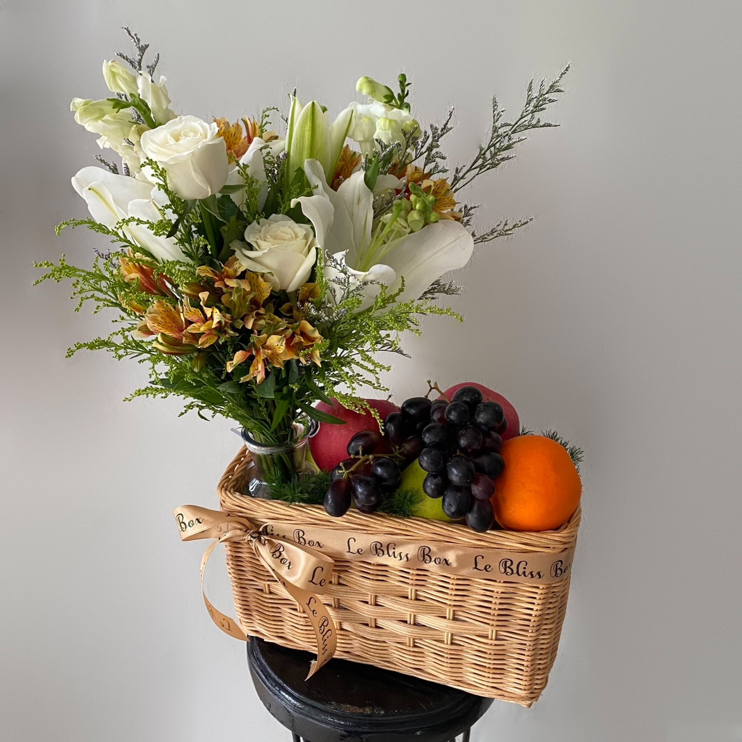 Basket with flowers, fruits, and a bottle on a gray background. Parcel buah surabaya by le bliss bouquet