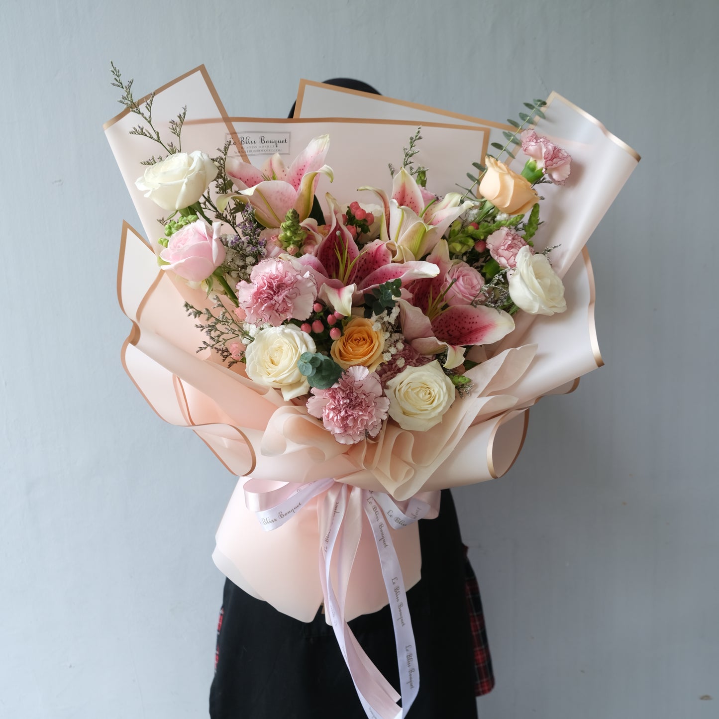 Bouquet of flowers with pink ribbons held by a person against a light gray background/ FLORIST JAKARTA, FLORIST SURABAYA, FLORIST CIREBON. LE BLISS BOUQUET
