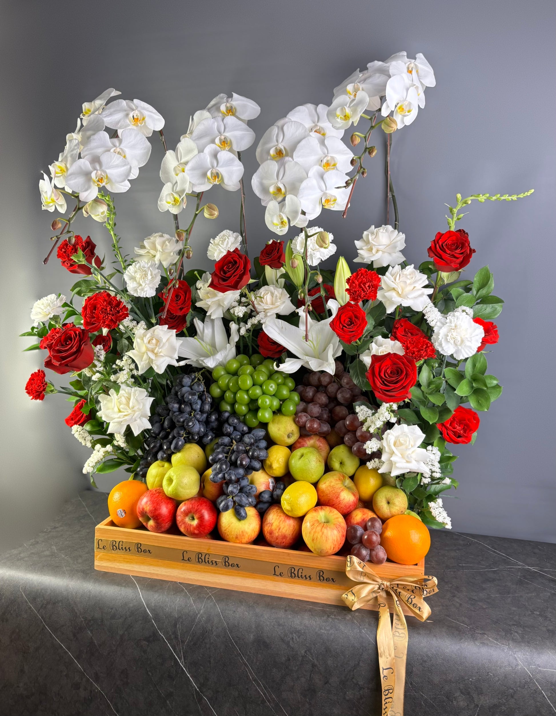Bouquet of flowers with red, white, and green colors displayed on a wooden fruit basket against a gray background. Parcel buah besar dengan anggrek, rangkaian bunga besar by le bliss box. parcel buah surabaya, jakarta, tangerang, gresik, surabaya, sidoarjo