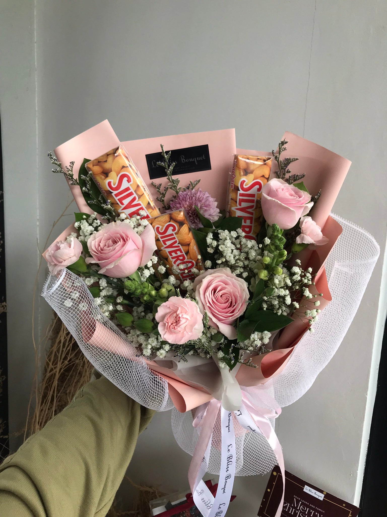 Bouquet of flowers with silverqueen chocolate bars wrapped in paper against a gray background. best florist in jakarta, surabaya, tangerang dan cirebon