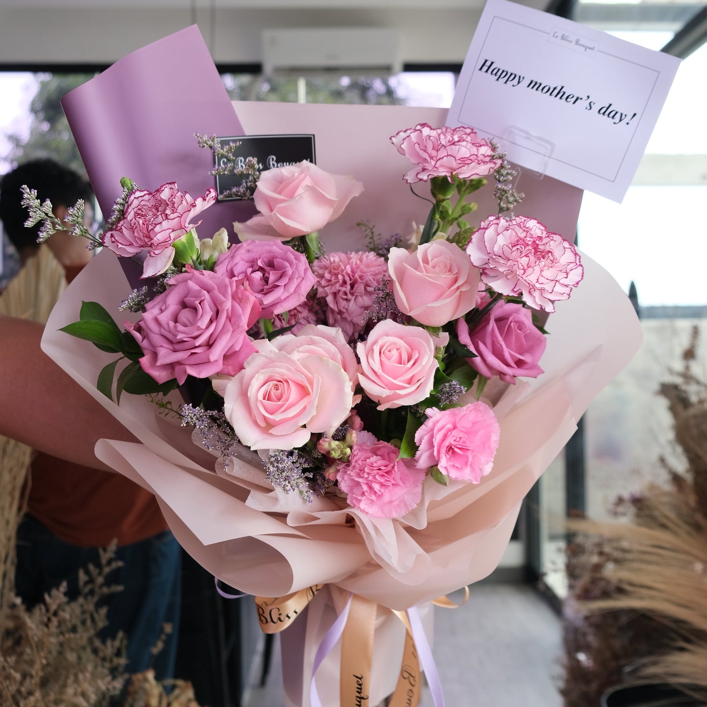 Bouquet of pink roses with a card on a reflective surface. Kado hari ibu, Pink Lilac Sonata Medium Bouquet dari Le Bliss Bouquet. Kado Hari Ibu yang elegan dengan mawar pink & lilac. Pengiriman Surabaya, Jakarta & Cirebon. Premium & heartfelt.