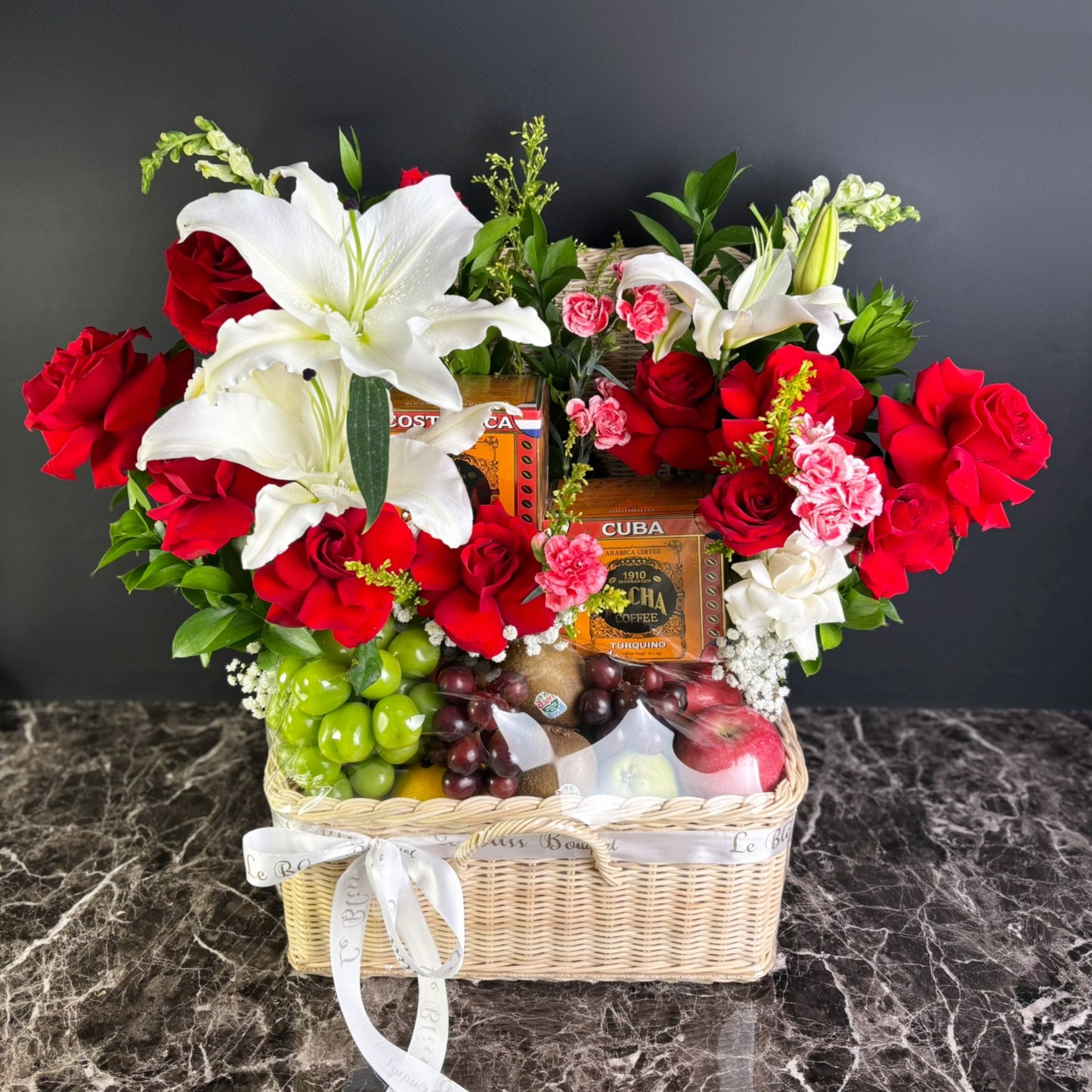 Bouquet of red and white flowers with fruits and cigars in a basket on a dark surface. Parcel Buah bunga bacha coffee surabaya, fruit hamper with bacha coffee