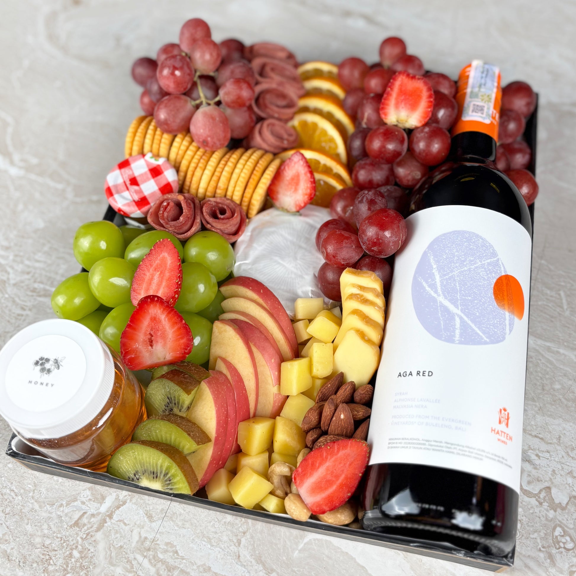 Charcuterie board with fruits, cheeses, and a bottle of wine on a light gray surface. Red Wine Cheese Platter with artisanal cheeses, fresh fruits, honey, jam & smoked beef. 