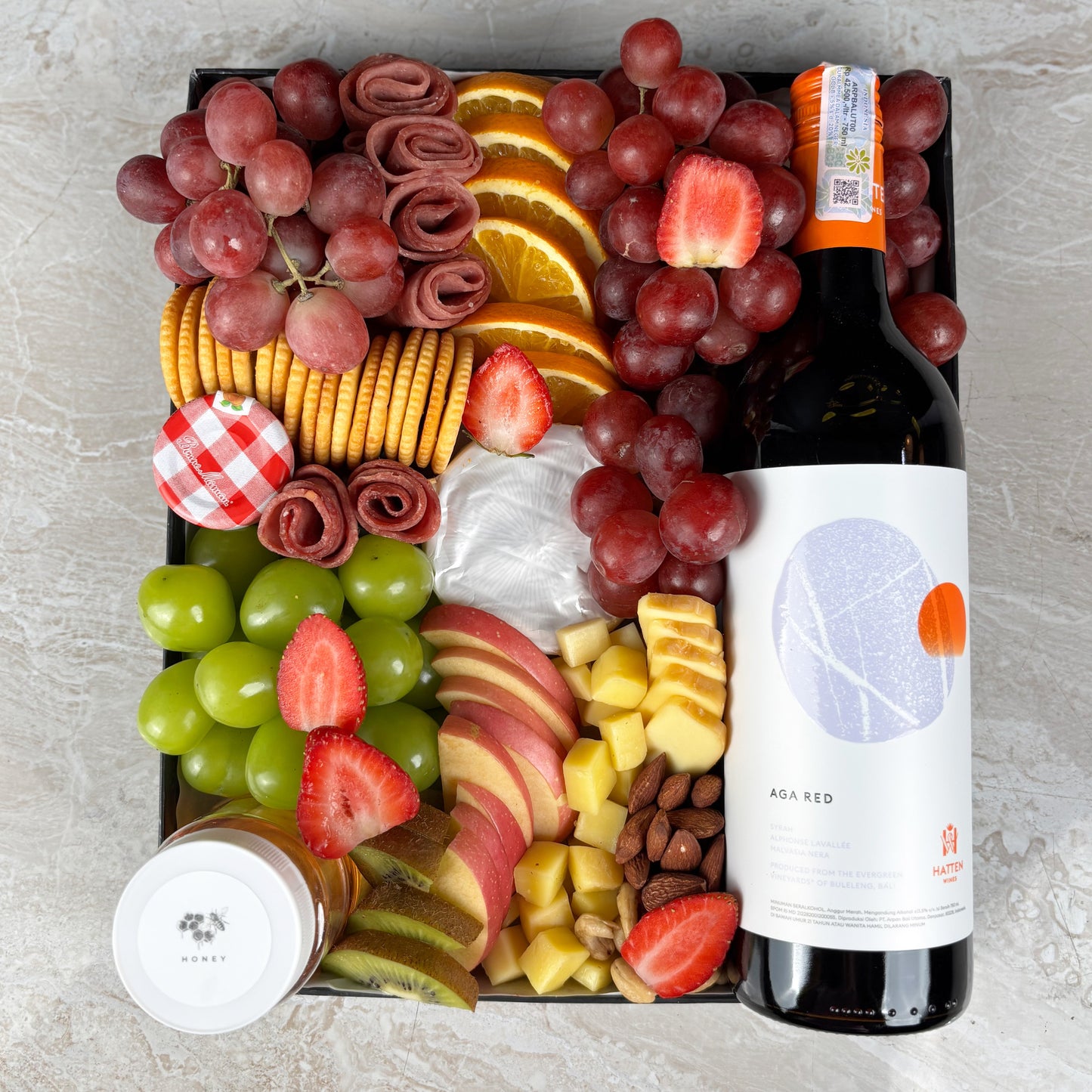 Charcuterie board with fruits, cheeses, and a bottle of wine on a light gray surface. Red Wine Cheese Platter with artisanal cheeses, fresh fruits, honey, jam & smoked beef. Perfect for gifting, celebrations, and premium grazing. Same-day delivery.