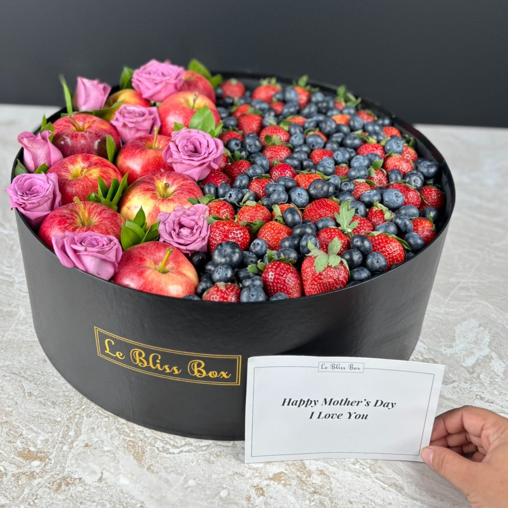 Decorative box filled with fruits and flowers, including apples, strawberries, and blueberries, with a 'Happy Mother's Day' card. kado hari ibu surabaya, jakarta, cirebon