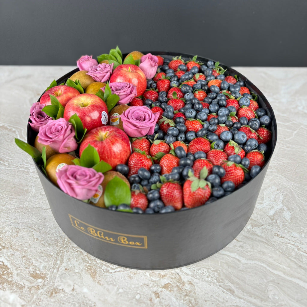 Decorative box filled with fruits and flowers on a light surface. Premium Apple, Kiwi & Berries Round Fruit Box dari Le Bliss Box. Parcel buah segar untuk hadiah mewah di Surabaya, Jakarta, Tangerang & Cirebon. Fresh, elegant, and healthy.