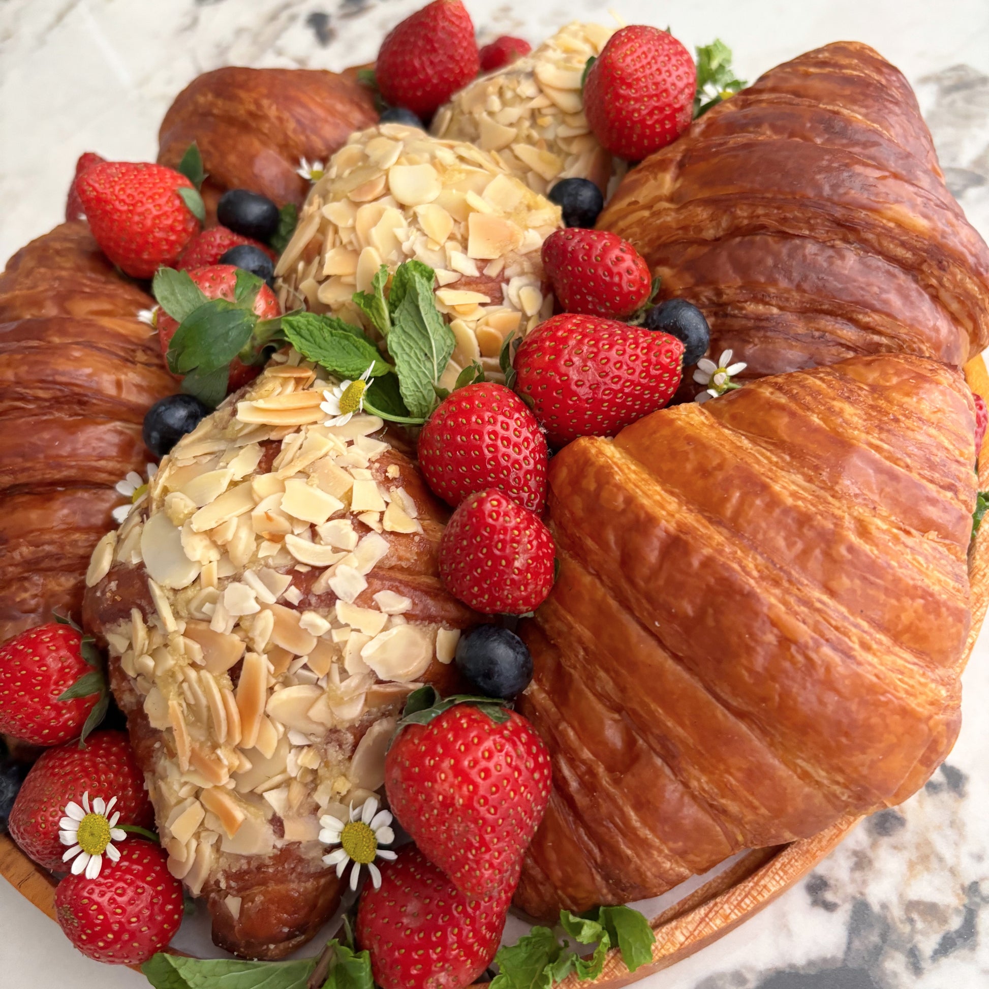 Decorative bread arrangement with croissants, almonds, and strawberries on a marble surface. platter jakarta, platter surabaya