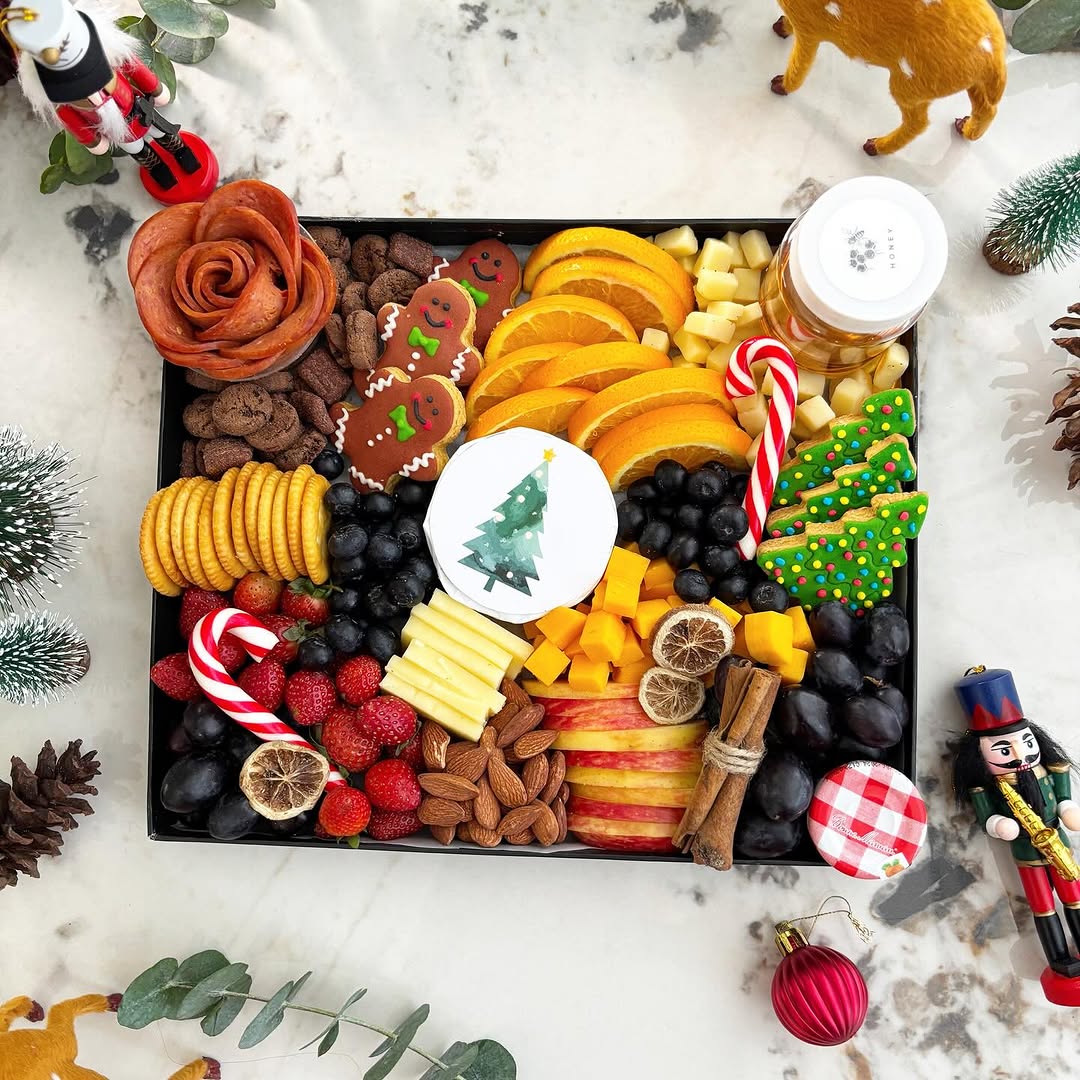 Decorative charcuterie board with fruits, cheeses, and cookies on a white surface with Christmas decorations. Celebrate the holidays with Le Bliss Platter’s Christmas Cheese Platter — elegant gourmet selection. Festive platter delivery in Jakarta & Surabaya.