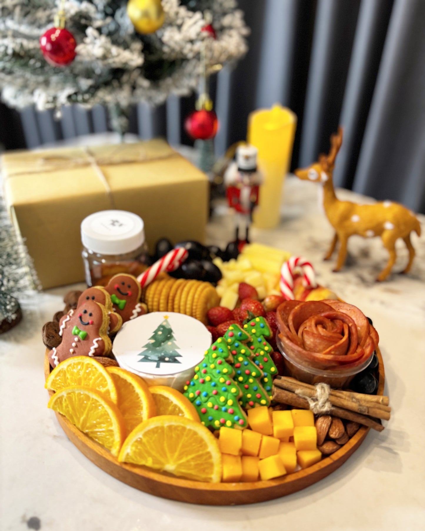 Decorative charcuterie board with fruits, cookies, and a small Christmas tree on a table with festive decorations.  festive charcuterie board with fruits, cheese, and meats on a marble surface. Christmas Round Cheese Platter | Christmas Platter Jakarta & Surabaya – Le Bliss Platter
