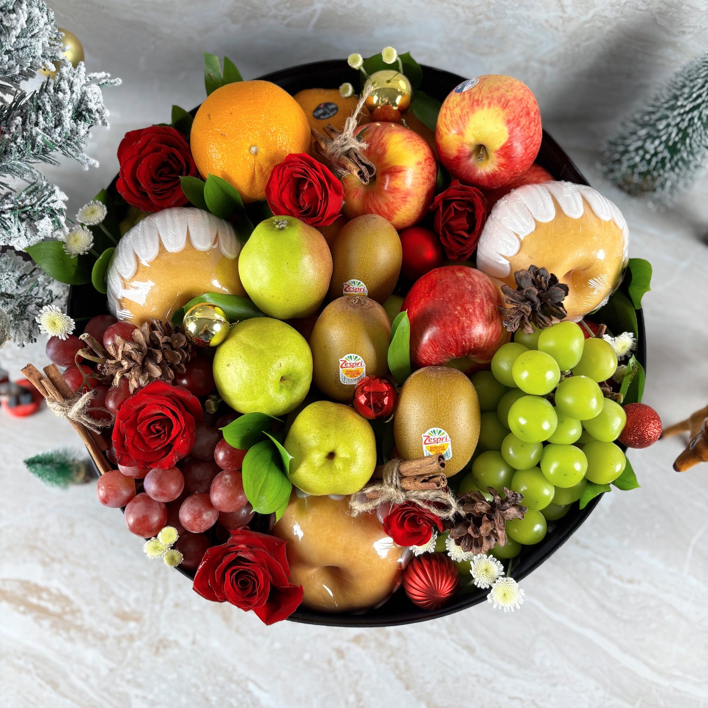 Decorative fruit and flower arrangement with apples, oranges, and roses on a white surface. PARCEL BUAH NATAL, HAMPER NATAL JAKARTA, HAMPER NATAL SURABAYA