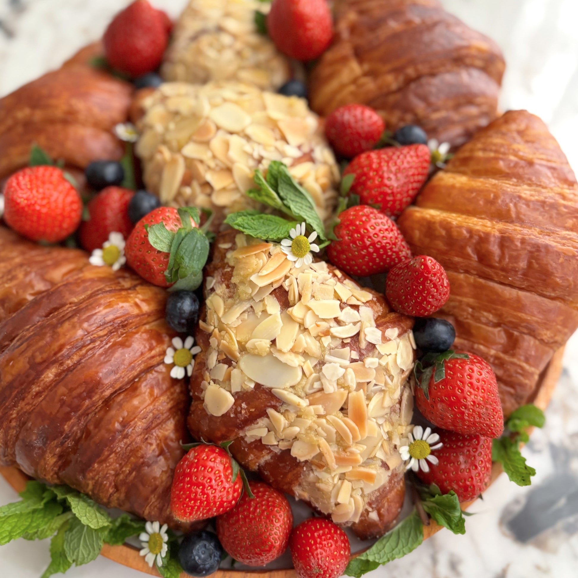 Decorative wreath made of croissants and pastries with strawberries and blueberries on a white background.  with croissants, almonds, and strawberries on a marble surface. platter jakarta, platter surabaya