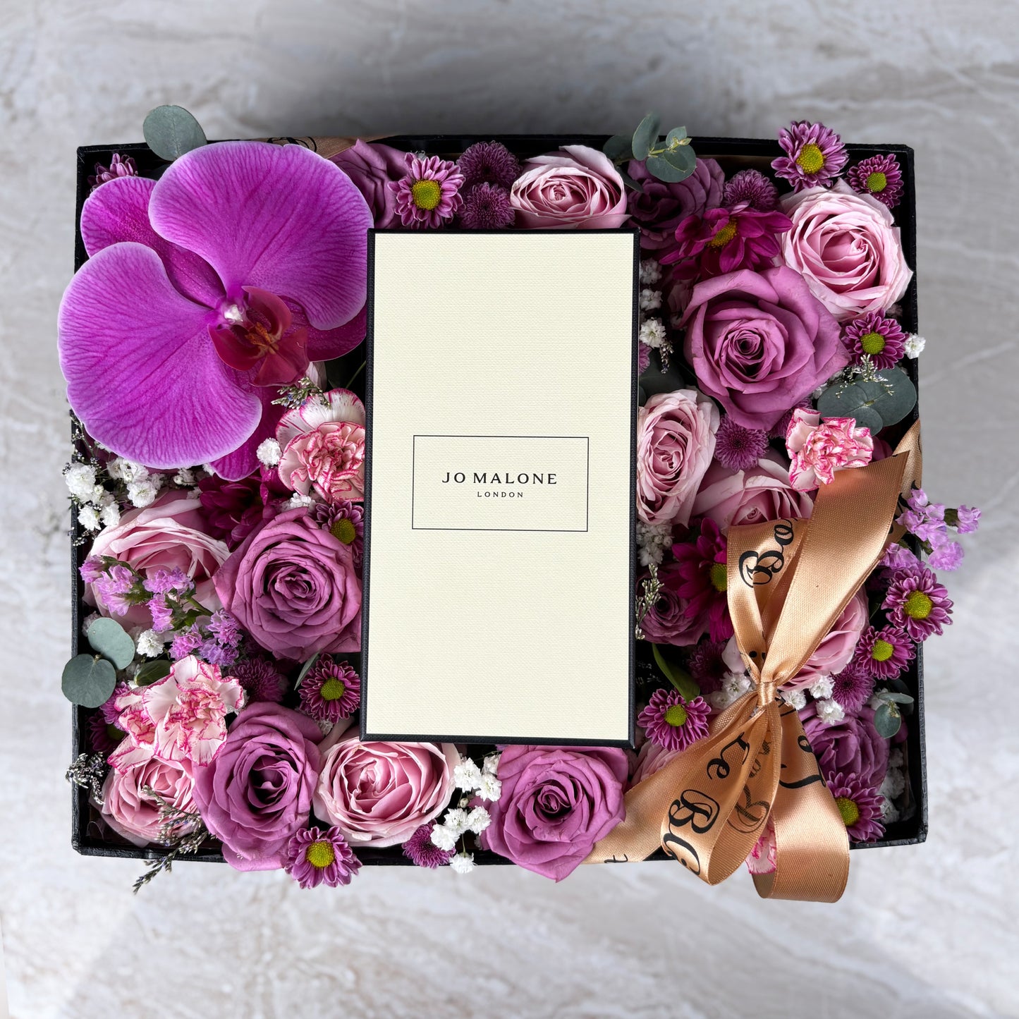 Floral arrangement in a box with Jo Malone branding on a white background. Floral arrangement with a Jo Malone perfume bottle in a decorative box. Kado Hari Ibu Surabaya, Kado Hari Ibu Jakarta