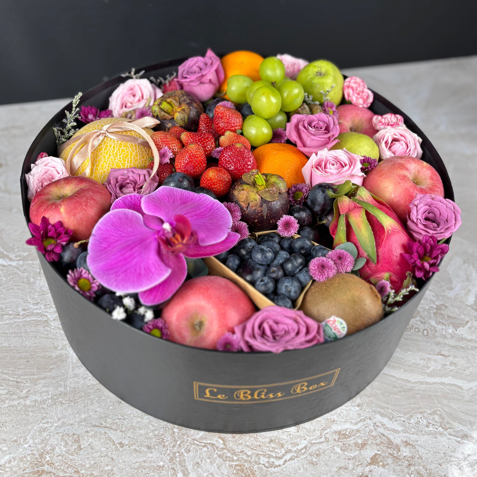 Fruit and flower arrangement in a black box labeled 'Le Bliss Box' on a light surface. Parcel Buah surabaya, parcel buah jakarta, parcel buah tangerang