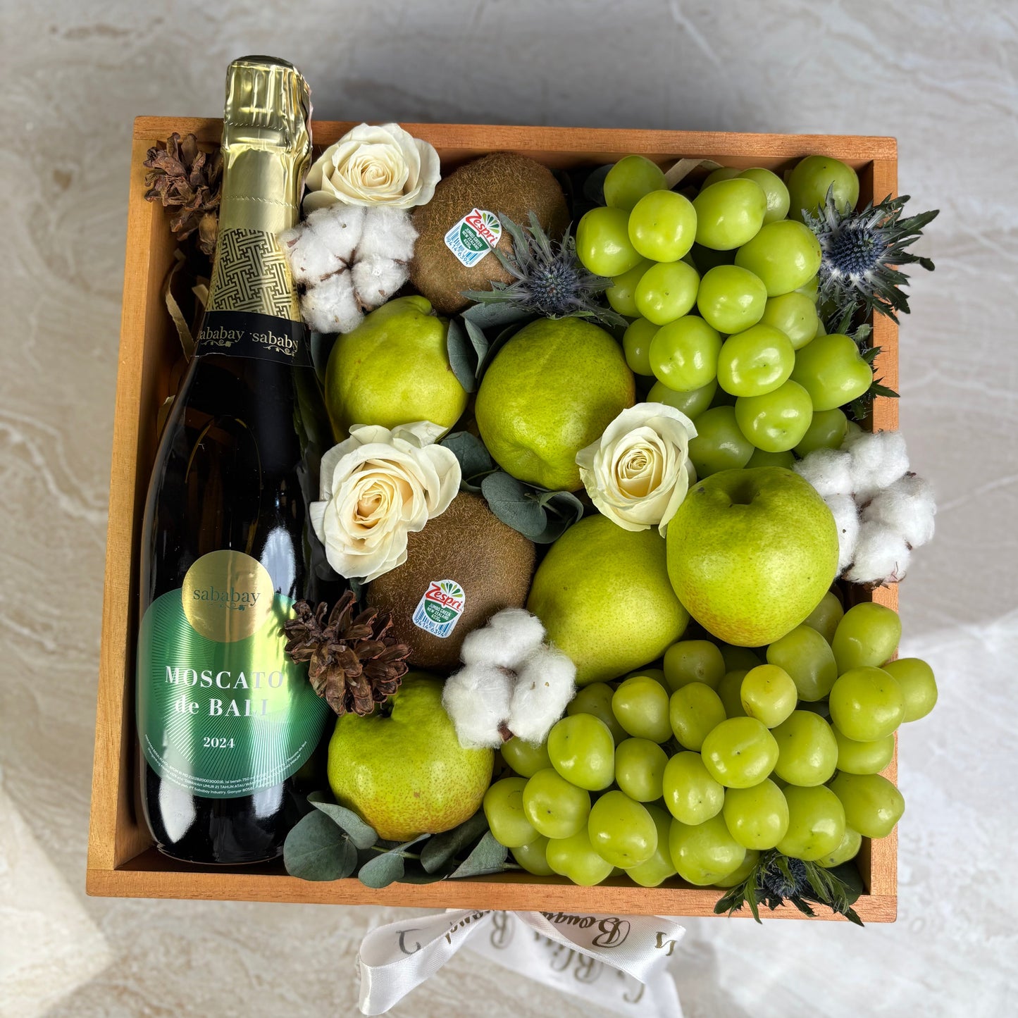 Fruit and wine gift basket with apples, grapes, and a bottle of Moscato Sababay on a marble surface. wine hamper jakarta