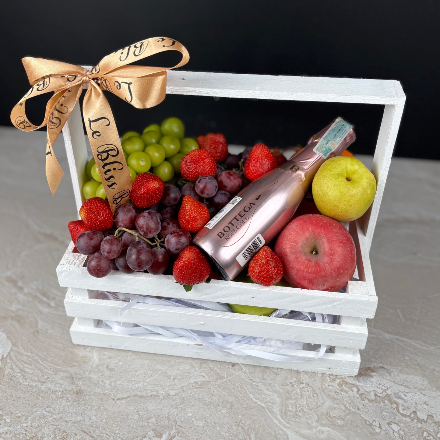 Fruit basket with a bottle of wine, apples, and berries on a white surface. le bliss box surabaya, jakarta, tangerang cirebon