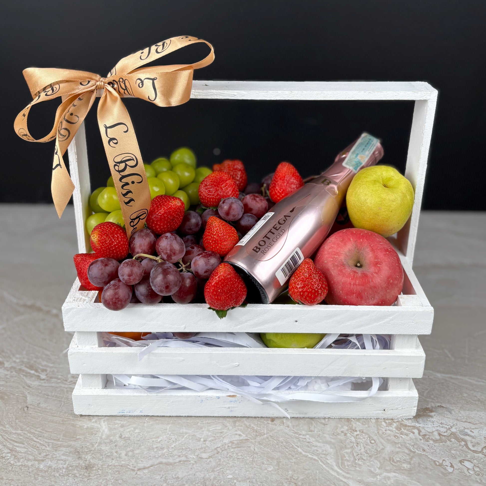 Fruit basket with a bottle of wine, grapes, strawberries, and apples on a white background. Fruit hamper with wine bottega jakarta, surabaya, cirebon