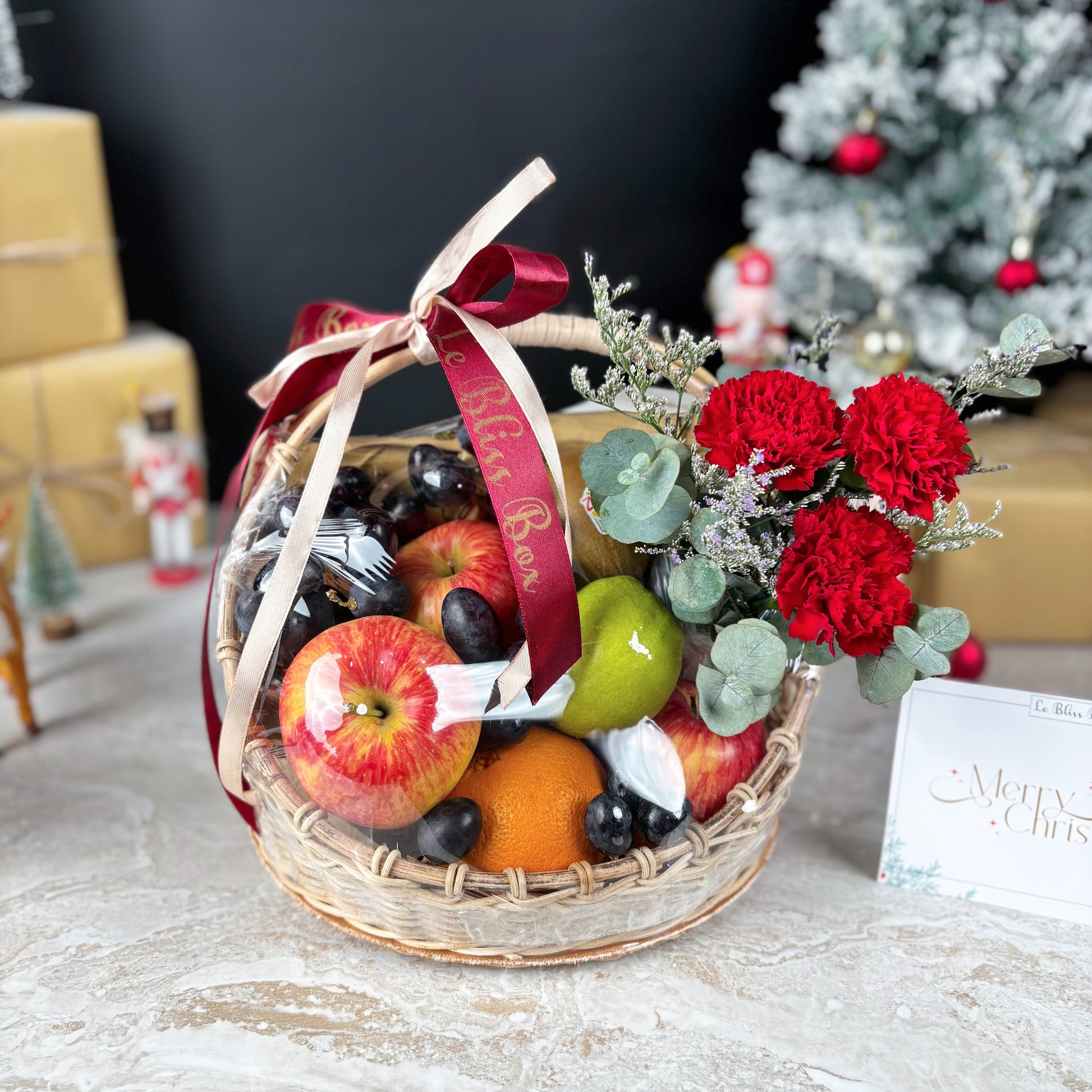 Fruit basket with flowers and a red ribbon on a festive background. Christmas Blossom Fruit Parcel | Best Christmas Hamper Jakarta, Tangerang, Cirebon & Surabaya – Le Bliss Bouquet