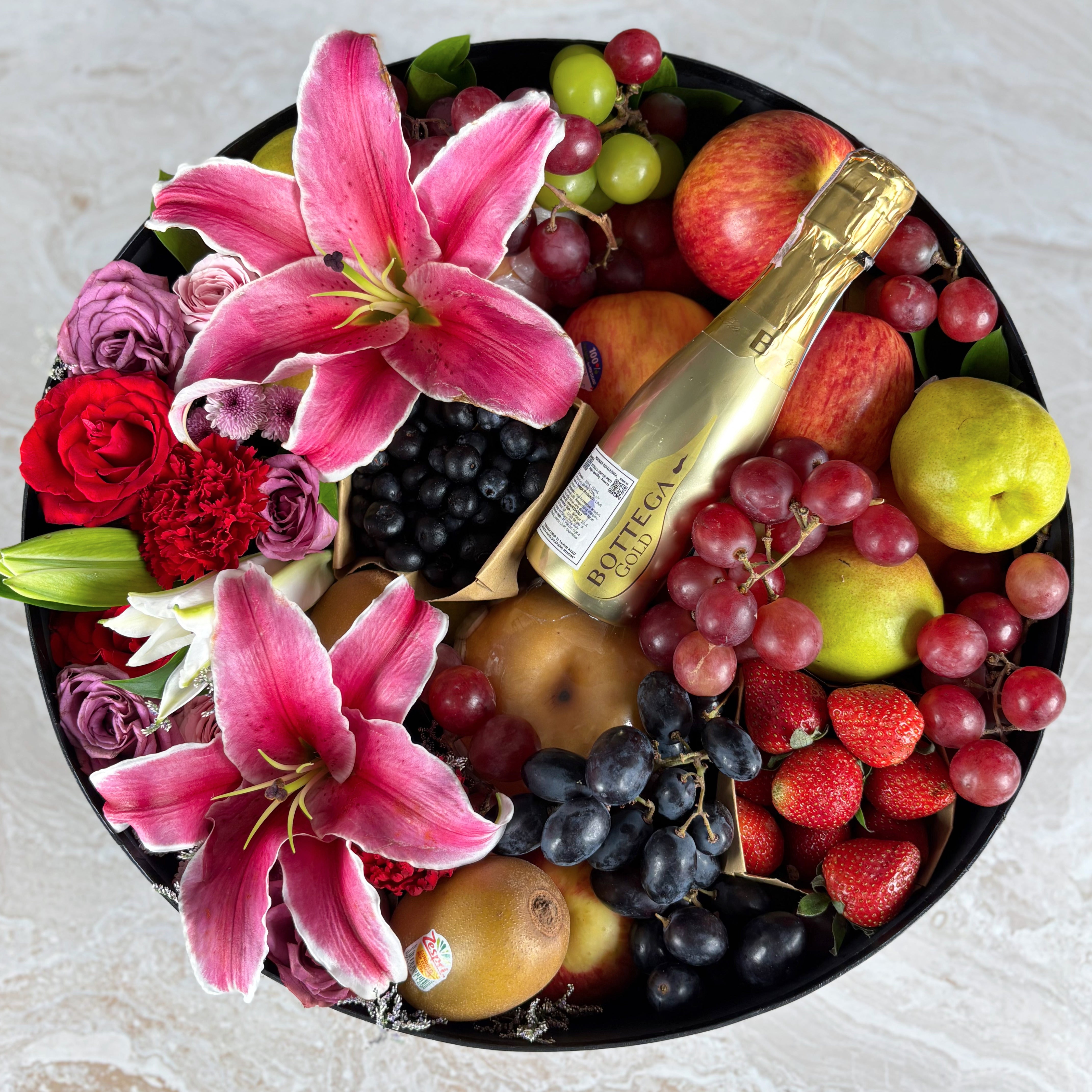 Fruit hamper with flowers and a bottle of champagne on a light background. Fruit basket with flowers and a bottle of champagne on a light surface. Bottega Grand Round Fruit Box | Best Wine Fruit Hamper in Jakarta, Surabaya & Tangerang – Le Bliss Box