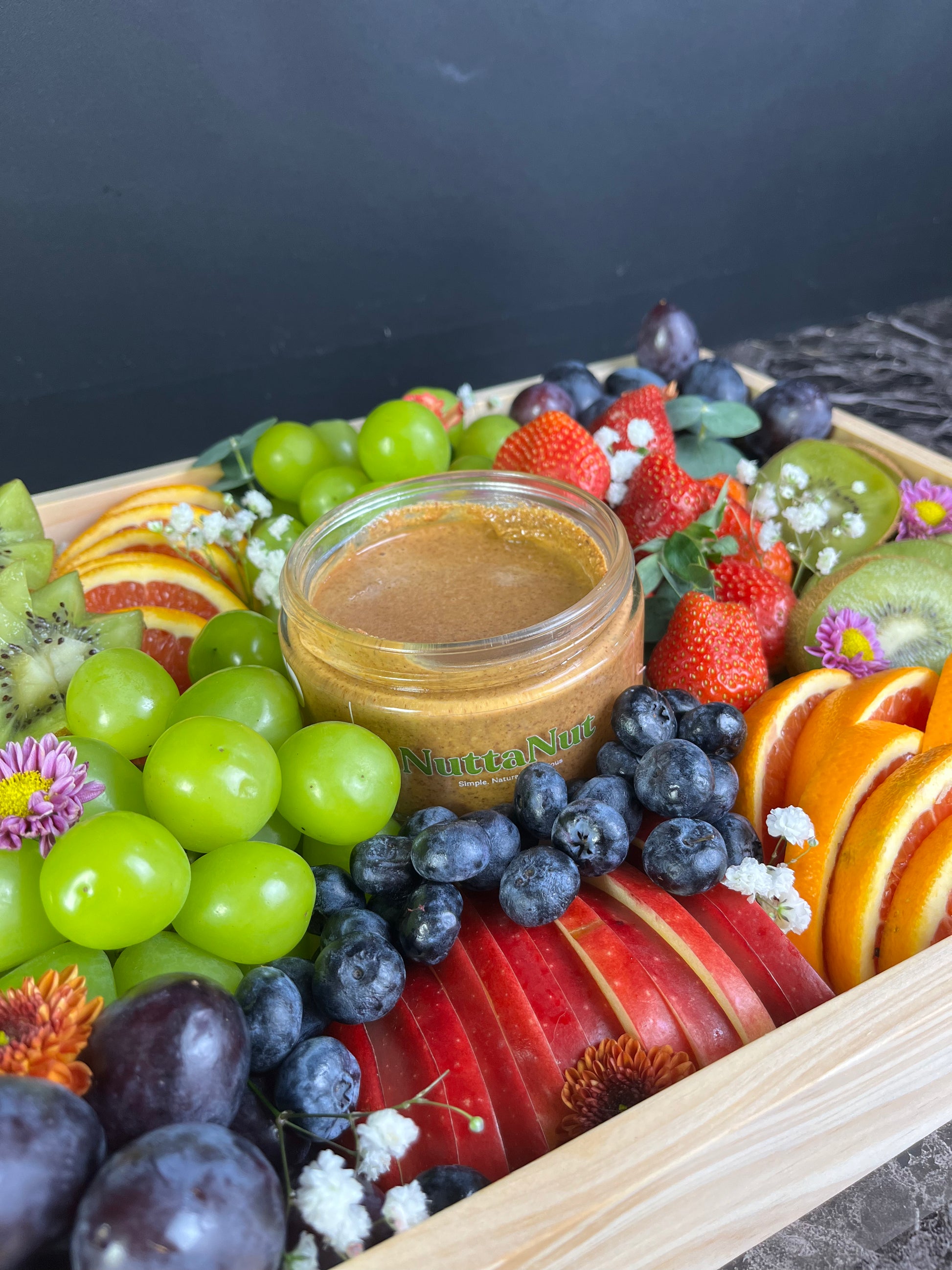 Fruit platter with a jar of almond butter from NuttaNut on a dark background