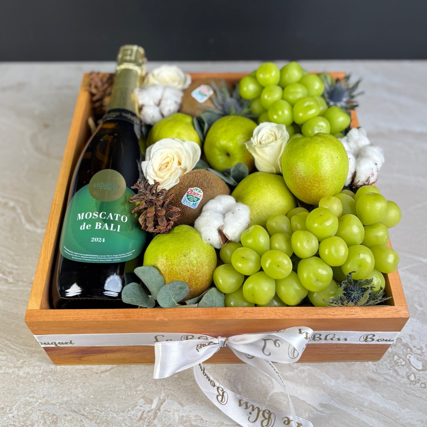 Gift basket with Moscato de Bali wine, fruits, and flowers on a light surface. wine hamper jakarta, wine hamper surabaya by le bliss box
