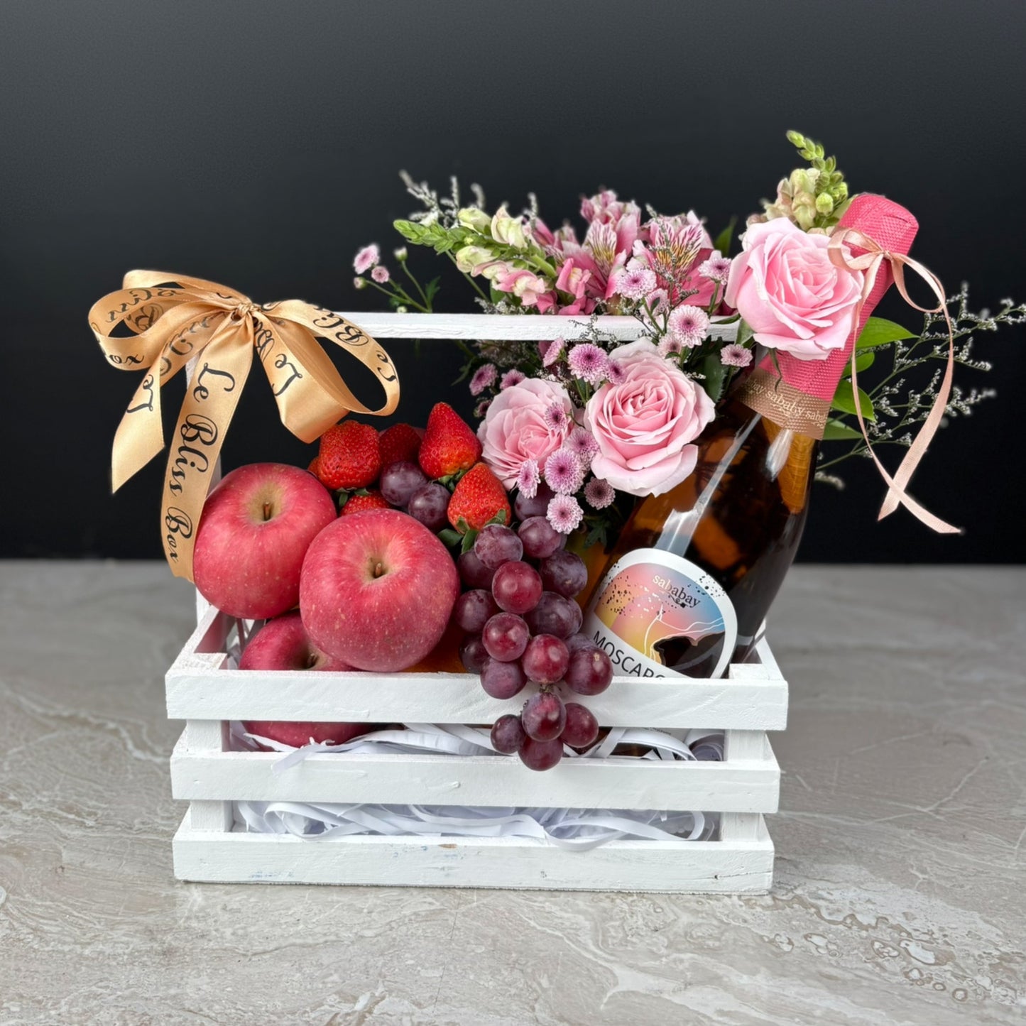 Gift basket with fruits, flowers, and a bottle of wine on a dark background. sababay wine hamper surabaya, jakarta, tangerang. fruit hamper with wine
