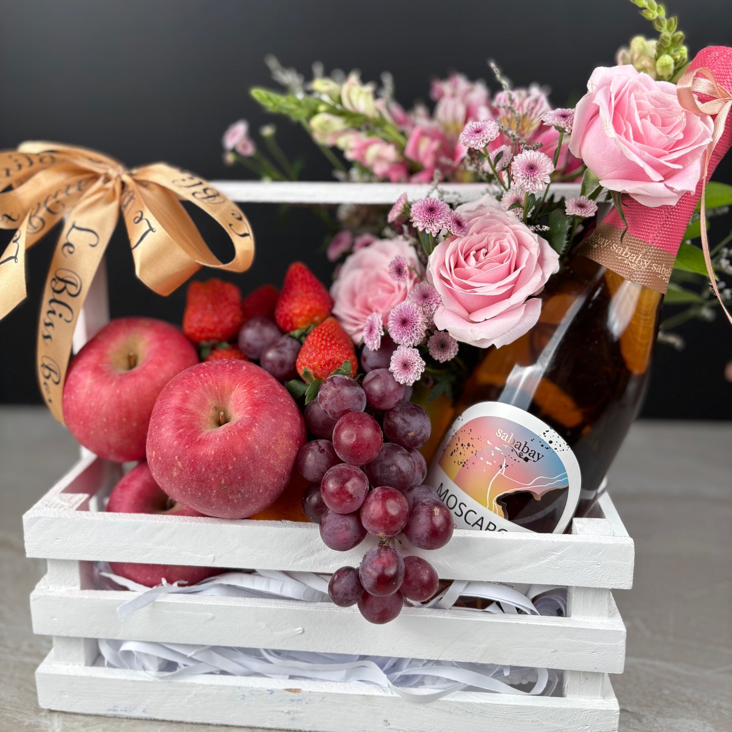 Gift basket with fruits, flowers, and a bottle of wine on a dark background. wine fruit hamper surabaya, jakarta