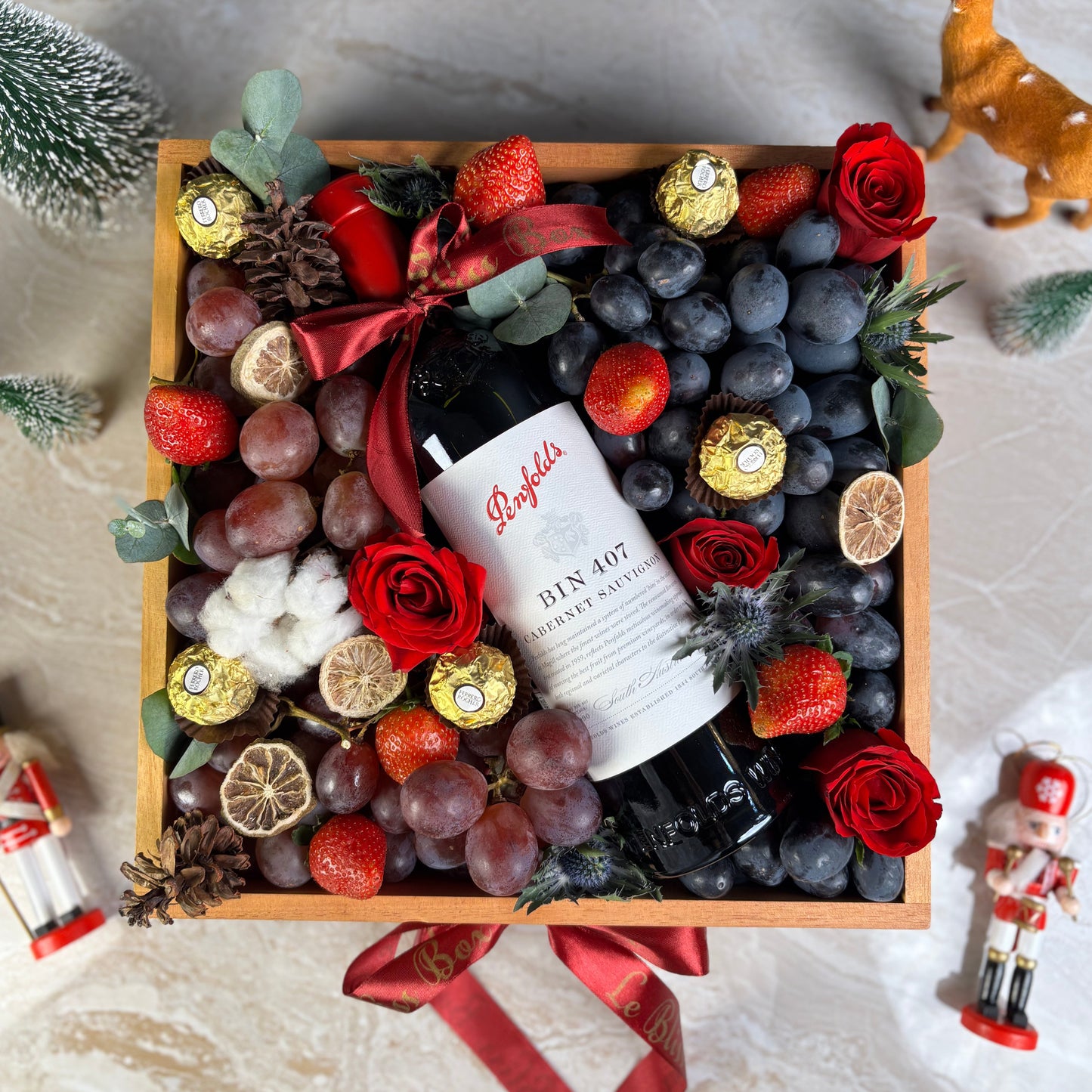Gift basket with fruits, flowers, and a bottle of wine on a textured surface. Penfolds Wine Hamper Jakarta, Surabaya. With Fresh autumn grapes, red globe grapes and strawberries and chocolate. Wine Hamper Jakarta. Christmas hamper jakarta