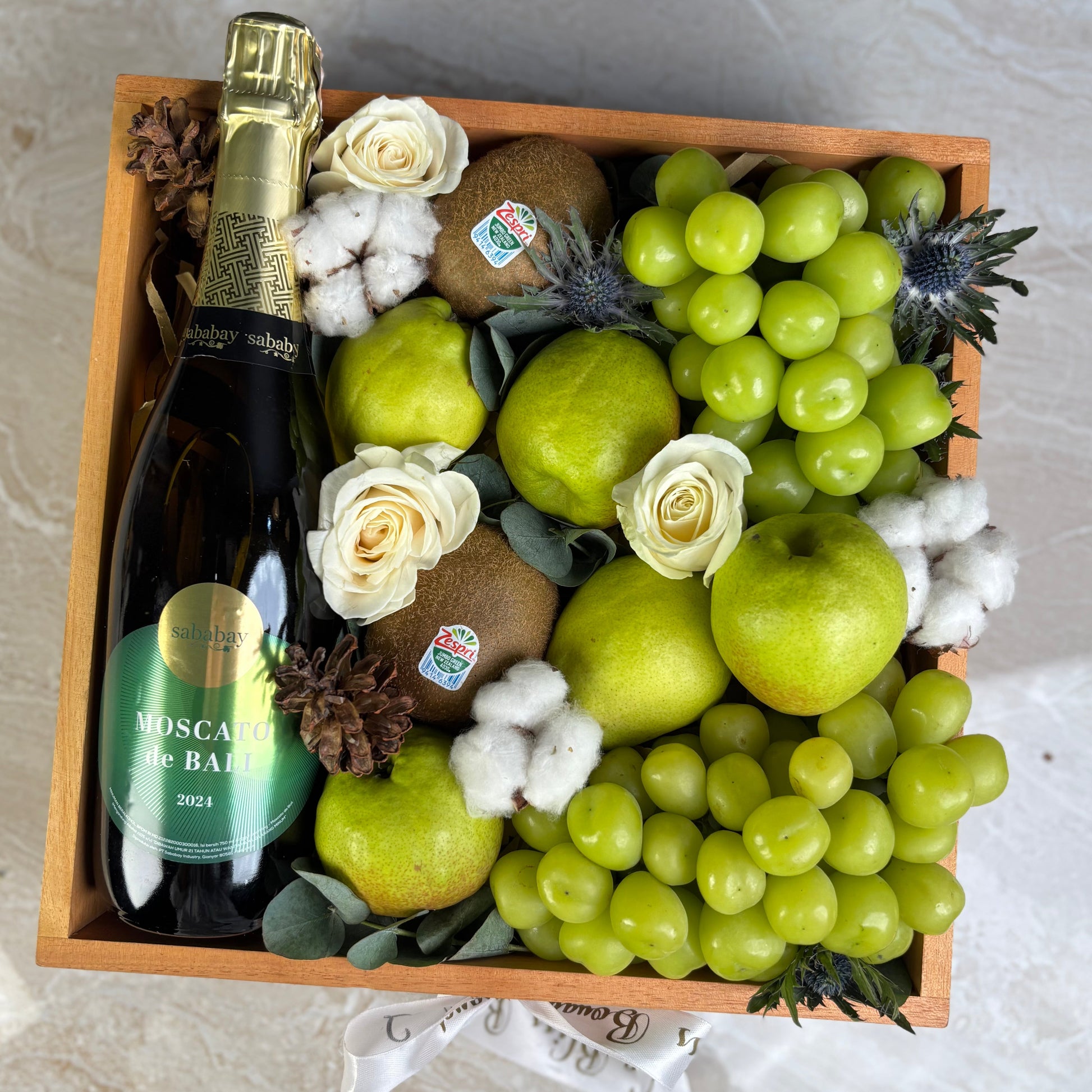 Gift basket with green apples, grapes, kiwis, and a bottle of Moscato on a marble surface. wine hamper jakarta