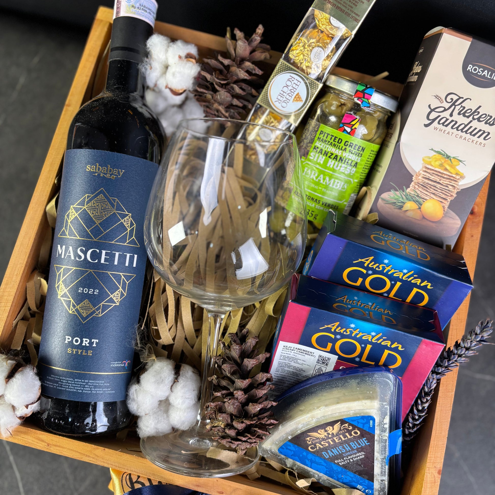 Gift basket with wine, cheese, and other snacks on a dark surface. Wine Hamper Jakarta, Surabaya. Gift basket with wine, cheese, and other snacks on a dark surface. By Le Bliss Box