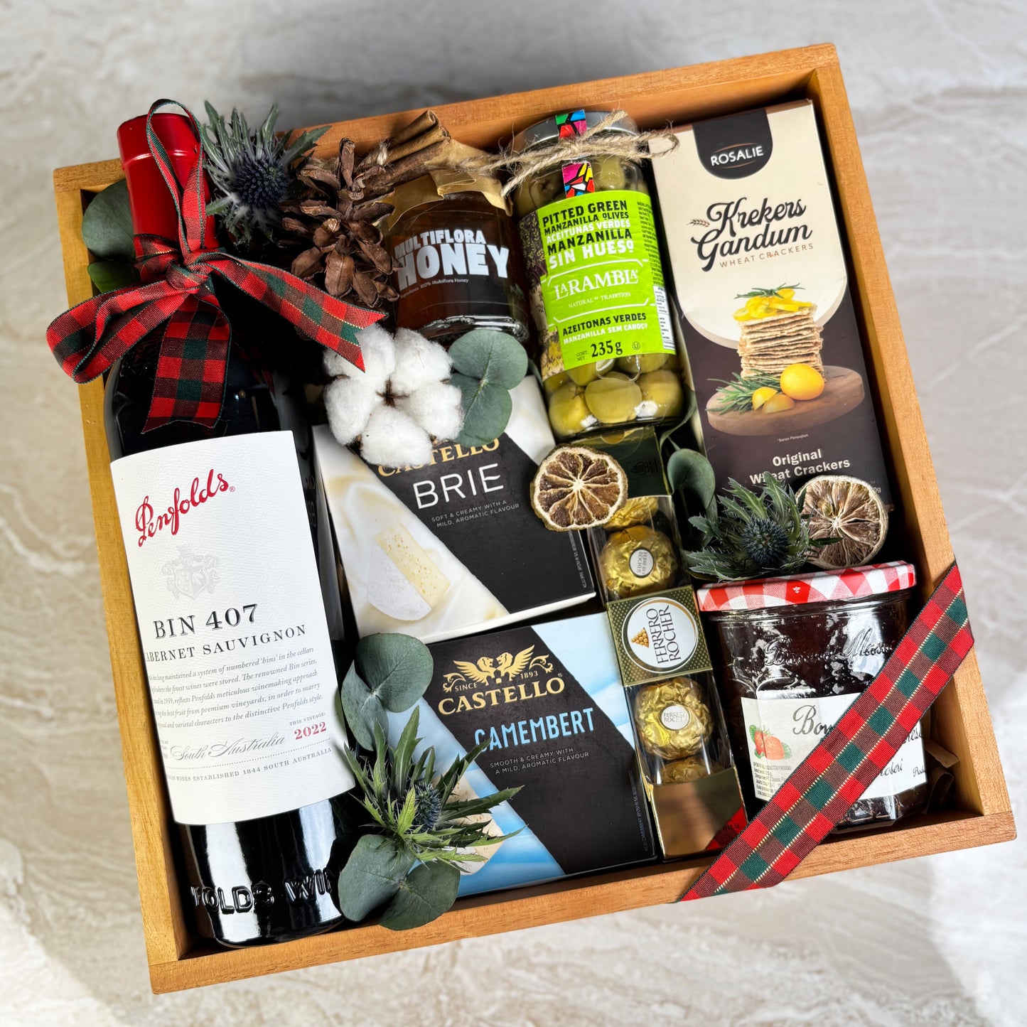 Gift basket with wine, cheese, and other snacks on a light background. Gift box with assorted foods and drinks including wine, cheese, and honey on a festive background. Gift basket with Penfolds wine, cheese, and other snacks on a textured surface. Gourmet Hamper Jakarta, Gourmet Hamper Surabaya, Christmas Hamper Jakarta, hamper natal jakarta, surabaya