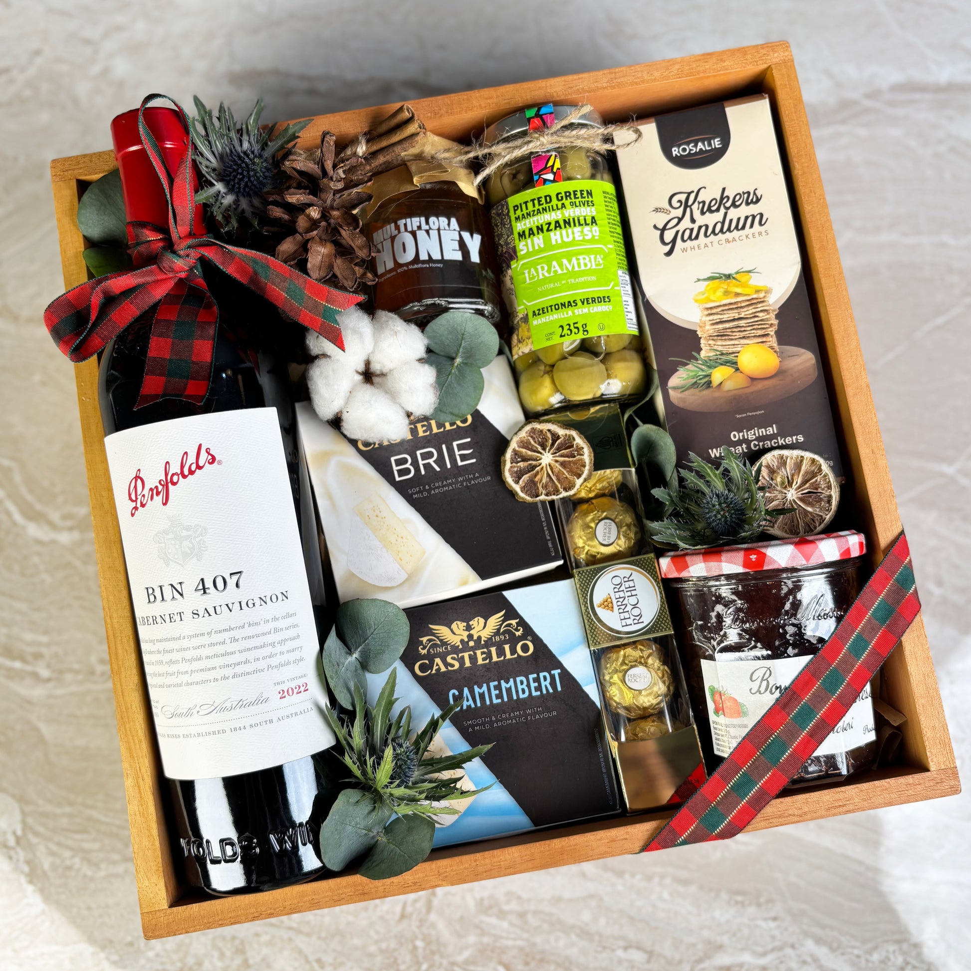 Gift basket with wine, cheese, and other snacks on a light background. Gift box with assorted foods and drinks including wine, cheese, and honey on a festive background. Gift basket with Penfolds wine, cheese, and other snacks on a textured surface. Gourmet Hamper Jakarta, Gourmet Hamper Surabaya, Christmas Hamper Jakarta, hamper natal jakarta, surabaya