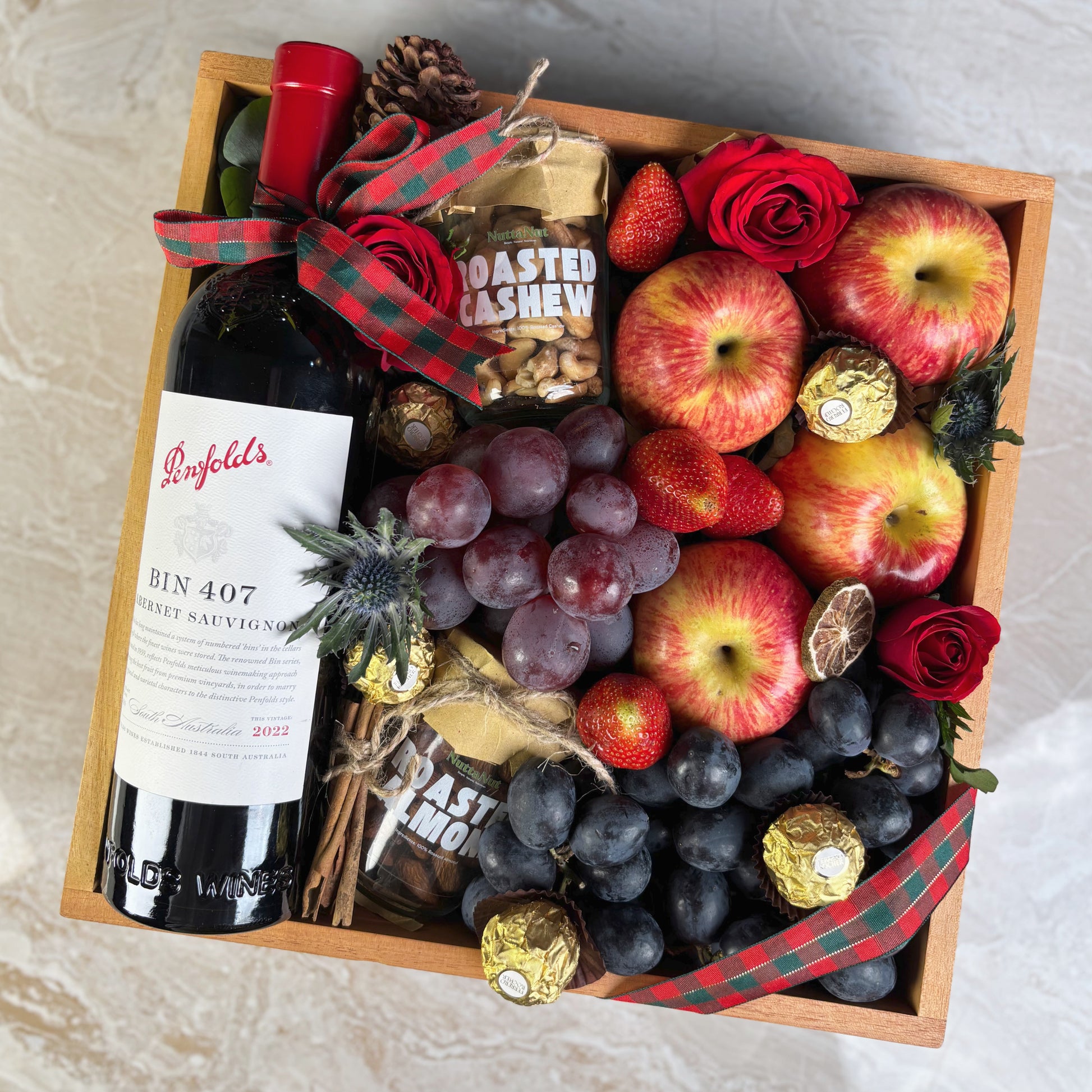 Gift box with Penfolds wine, fruits, and chocolates on a light background. Wine Hamper Jakarta by Le Bliss Box with roasted almond and cashew nuttanut. Penfolds Wine BIN 407 Hamper Jakarta