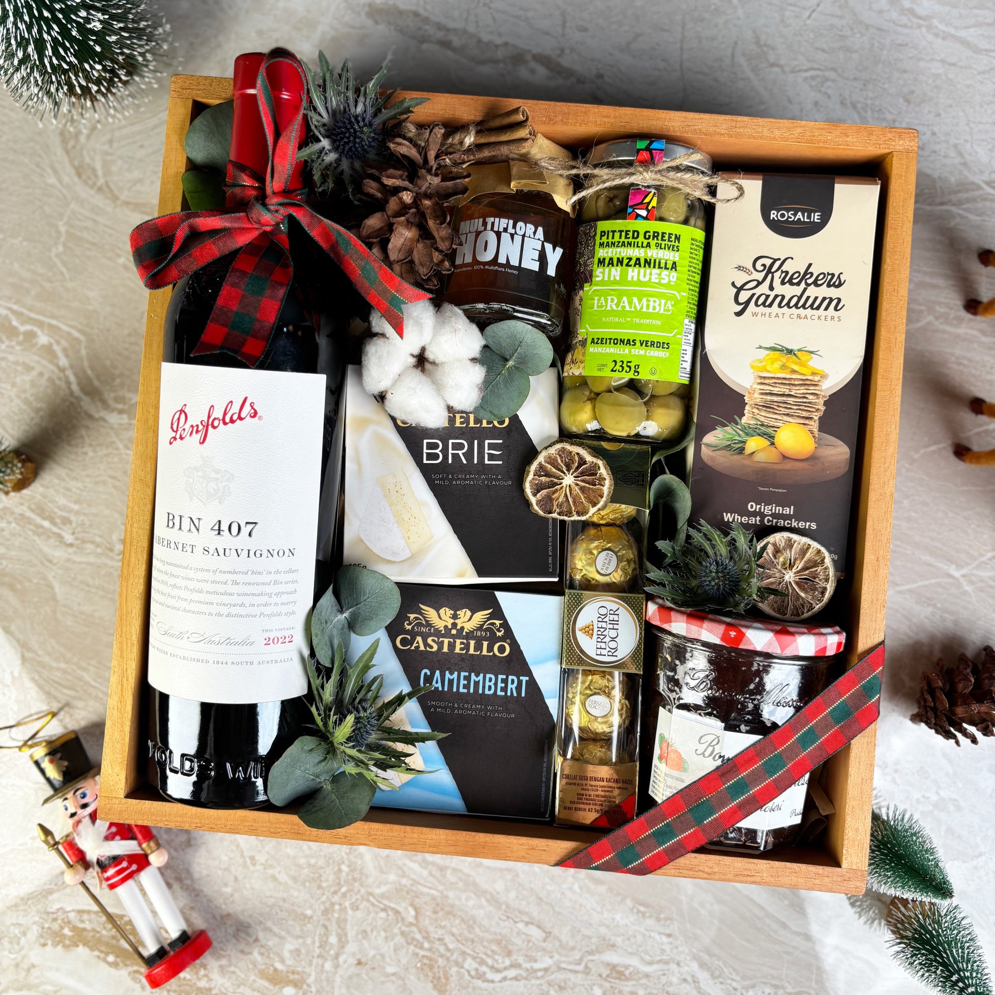 Gift box with assorted foods and drinks including wine, cheese, and honey on a festive background. Gift basket with Penfolds wine, cheese, and other snacks on a textured surface. Gourmet Hamper Jakarta, Gourmet Hamper Surabaya, Christmas Hamper Jakarta, hamper natal jakarta, surabaya