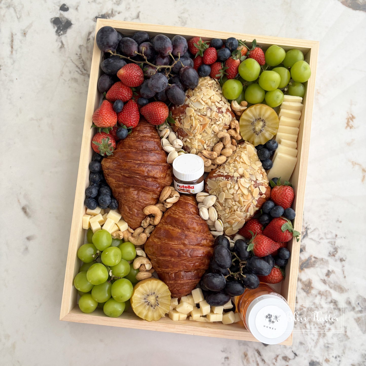 Gourmet platter with fruits, pastries, and cheeses on a marble surface. Wooden box filled with fruits, cheeses, and pastries on a marble surface. brunch platter jakarta, brunch platter surabaya, cheese platter jakarta. the best cheese platter and grazing service in jakarta by le bliss platter