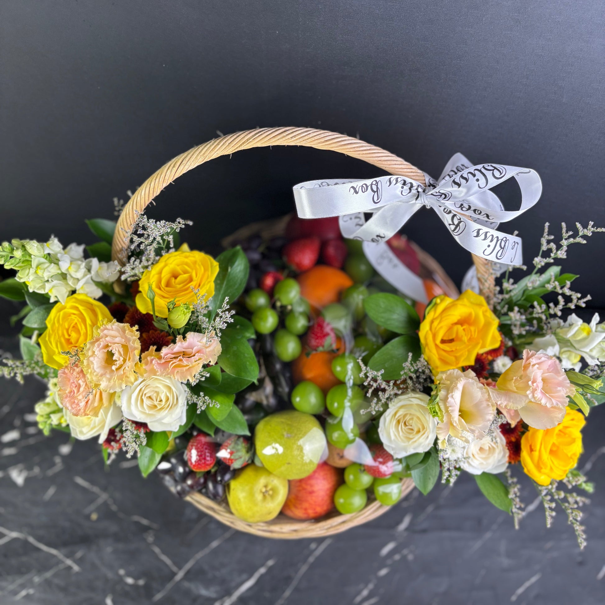 Basket filled with fruits and flowers on a dark surface