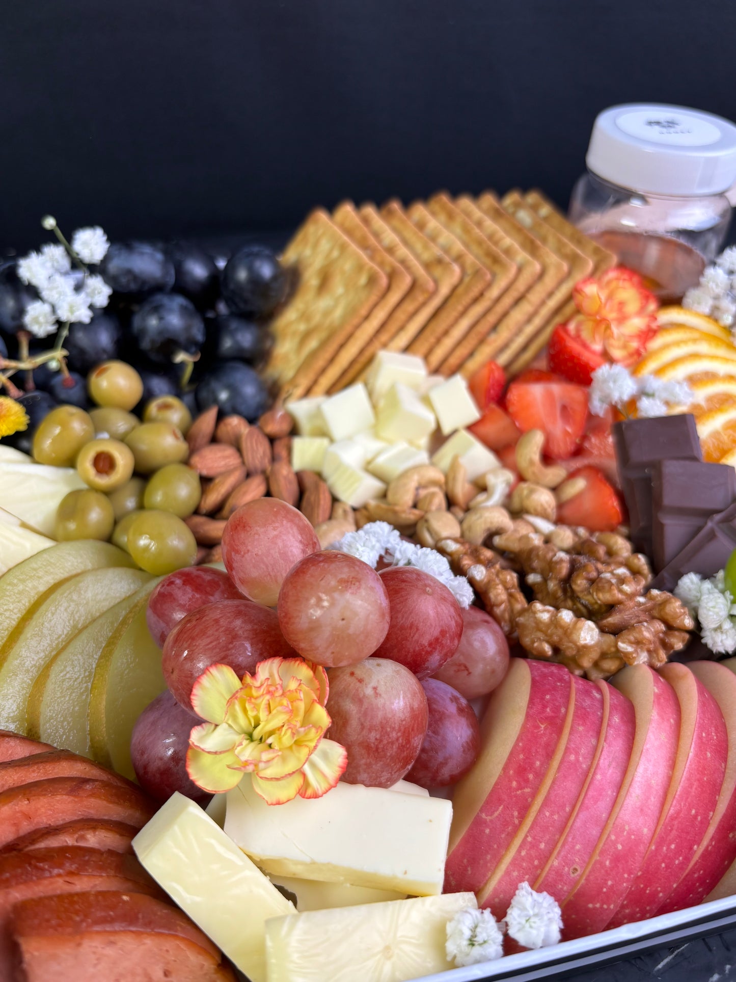 Assorted fruits, cheeses, and meats arranged on a platter with a black background.